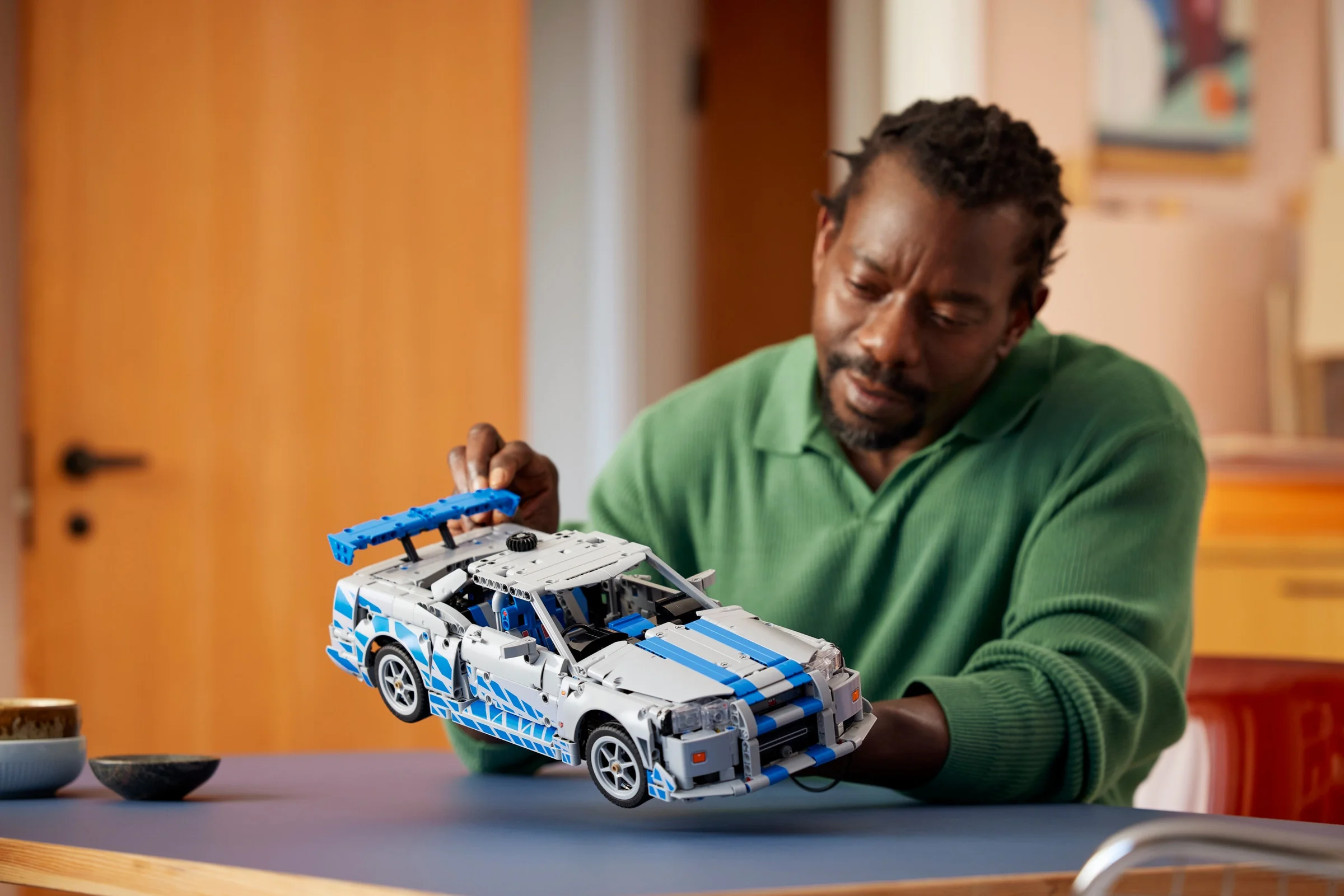 Un adult admiră mașina LEGO Nissan Skyline GT-R, o piesă detaliată și iconică.