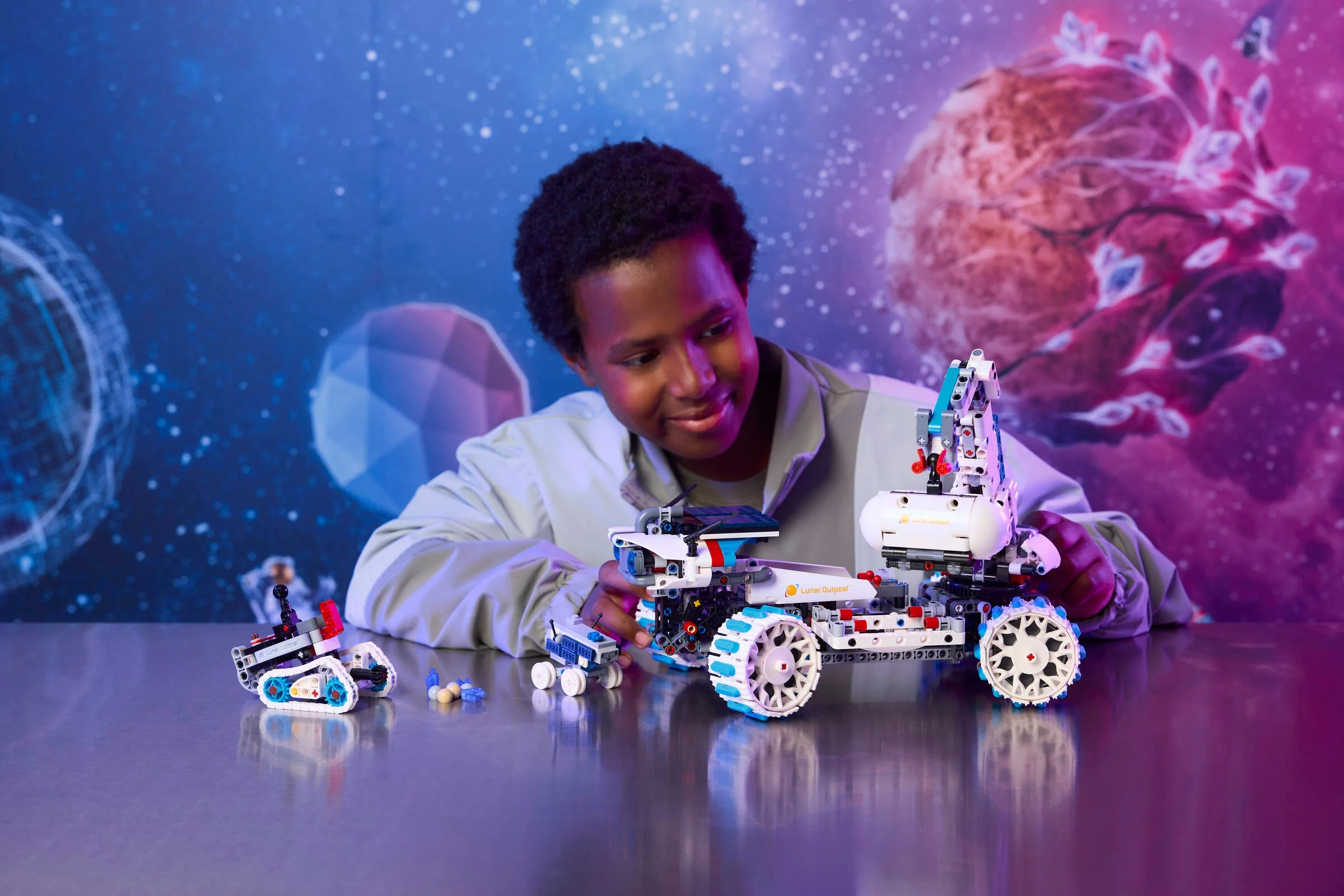 Un băiat se joacă cu roverul lunar LEGO Technic 42211. Fundal spațial colorat.