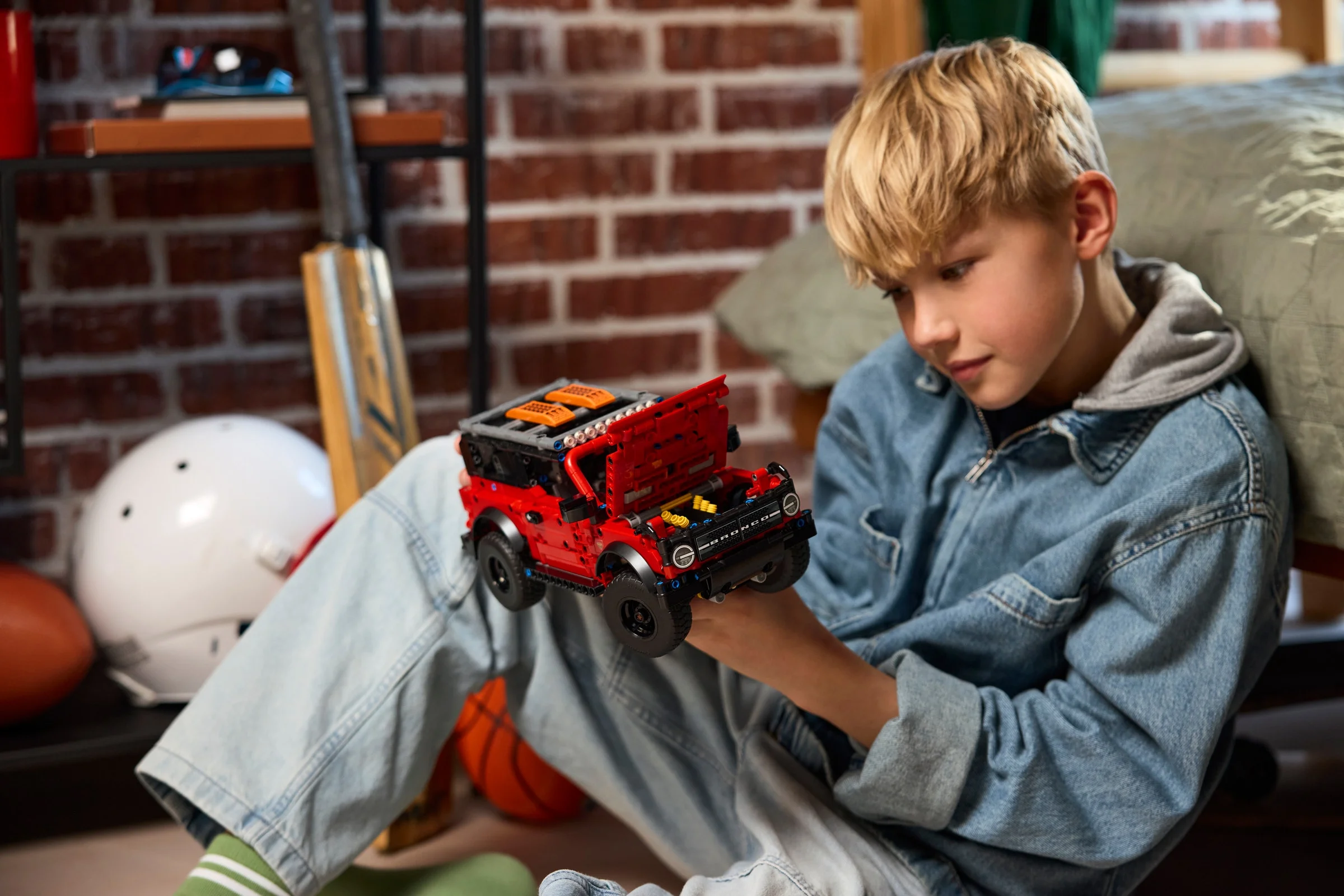 Un băiat se uită atent la modelul Ford Bronco LEGO Technic roșu.