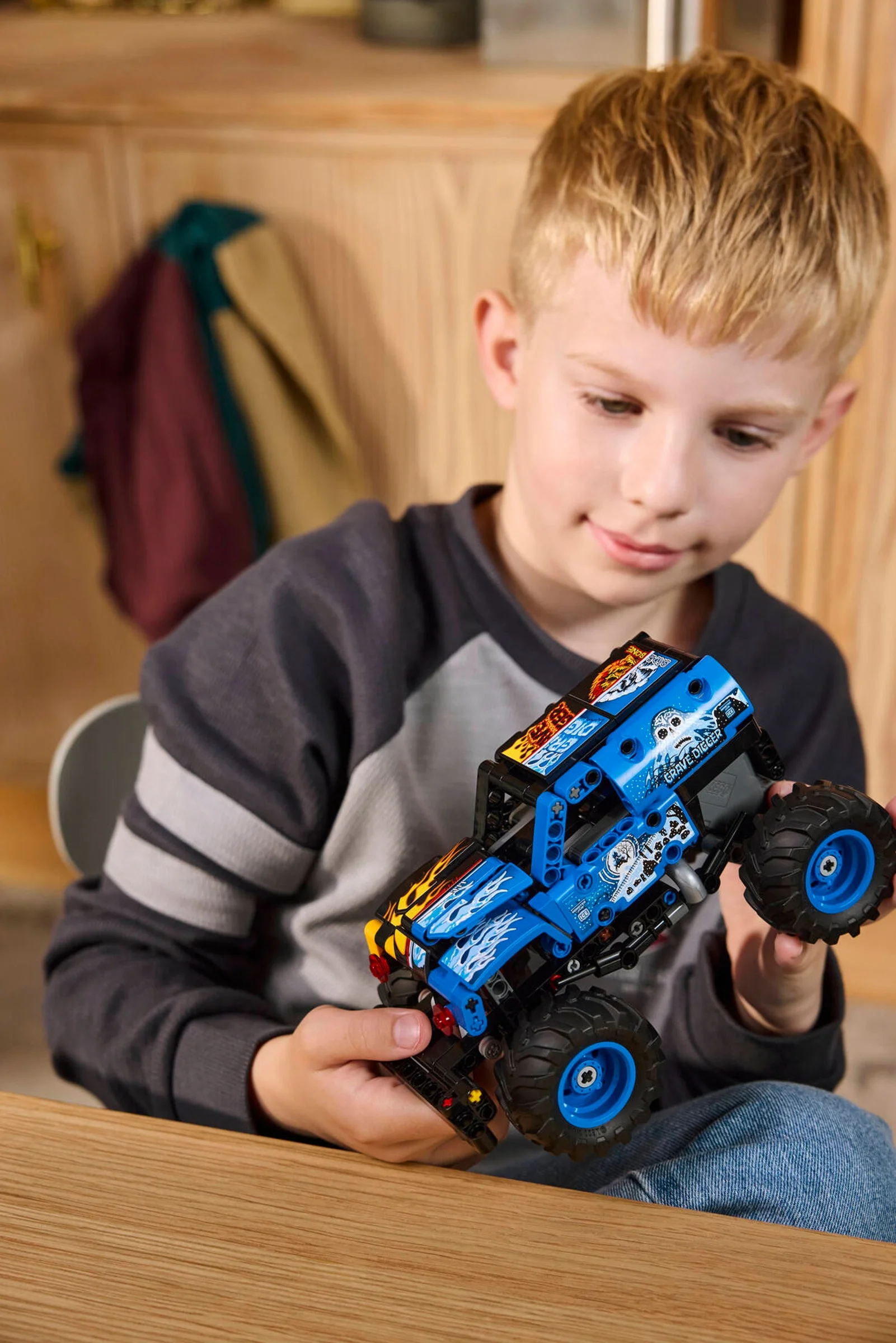 Un băiat se joacă cu modelul LEGO Technic Monster Jam Grave Digger. Modelul este albastru și negru.