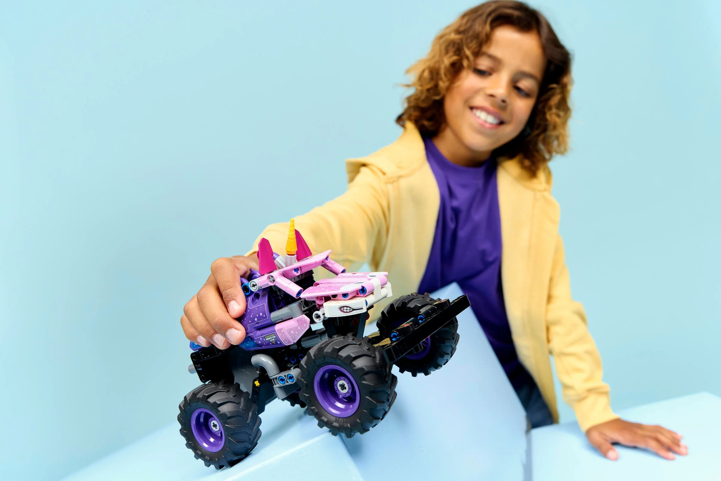 Un copil se joacă cu mașina Monster Jam Sparkle Smash. Zâmbetul îi luminează fața.