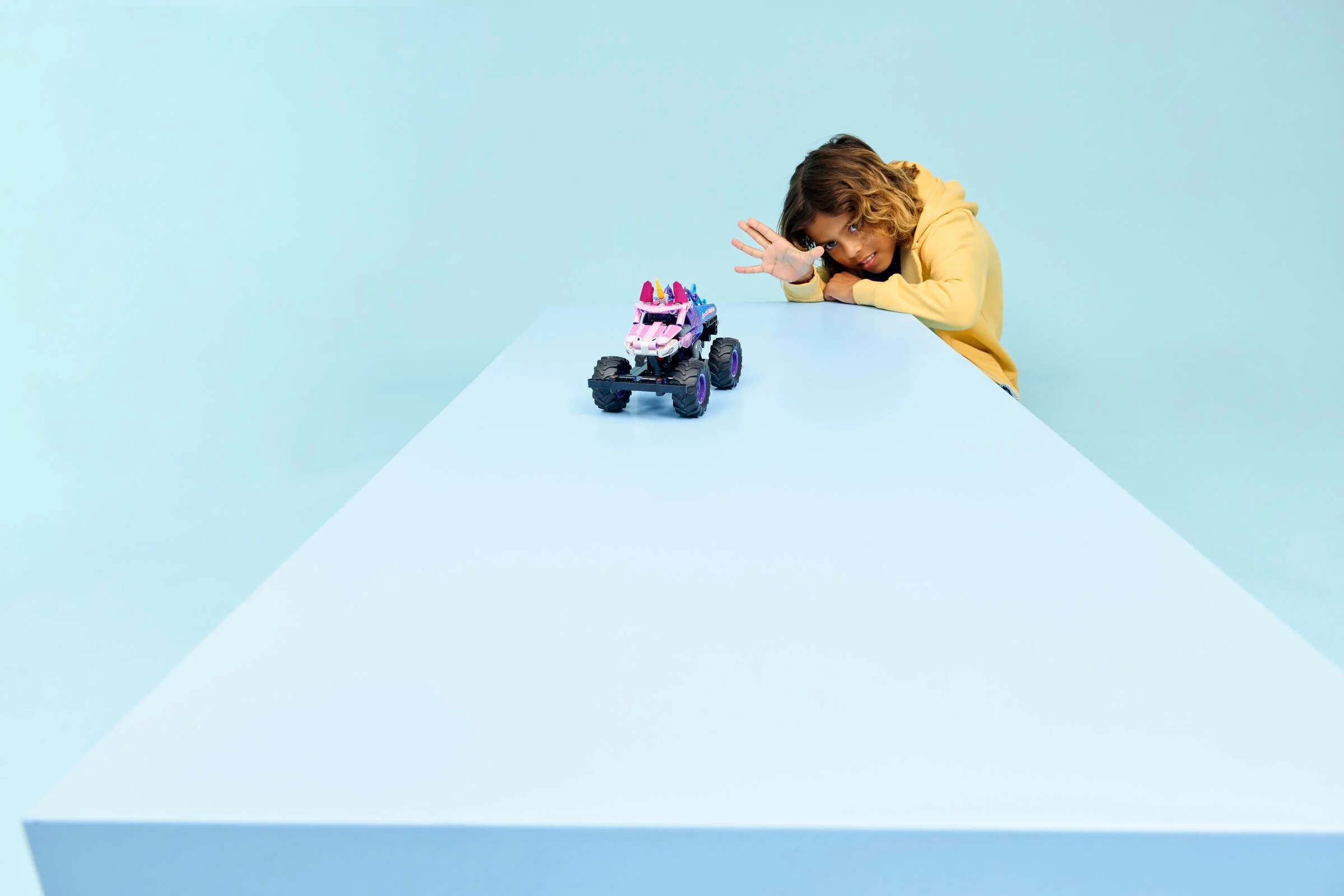 Un copil se uită la mașina Monster Jam Sparkle Smash pe o masă albastră.