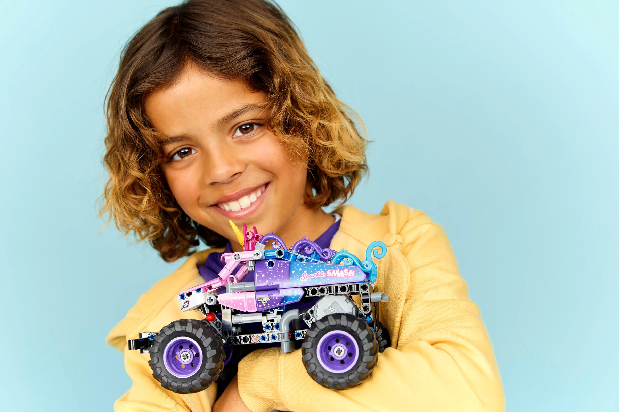 Copil zâmbitor ținând modelul LEGO Technic Monster Jam Sparkle Smash, viu colorat.