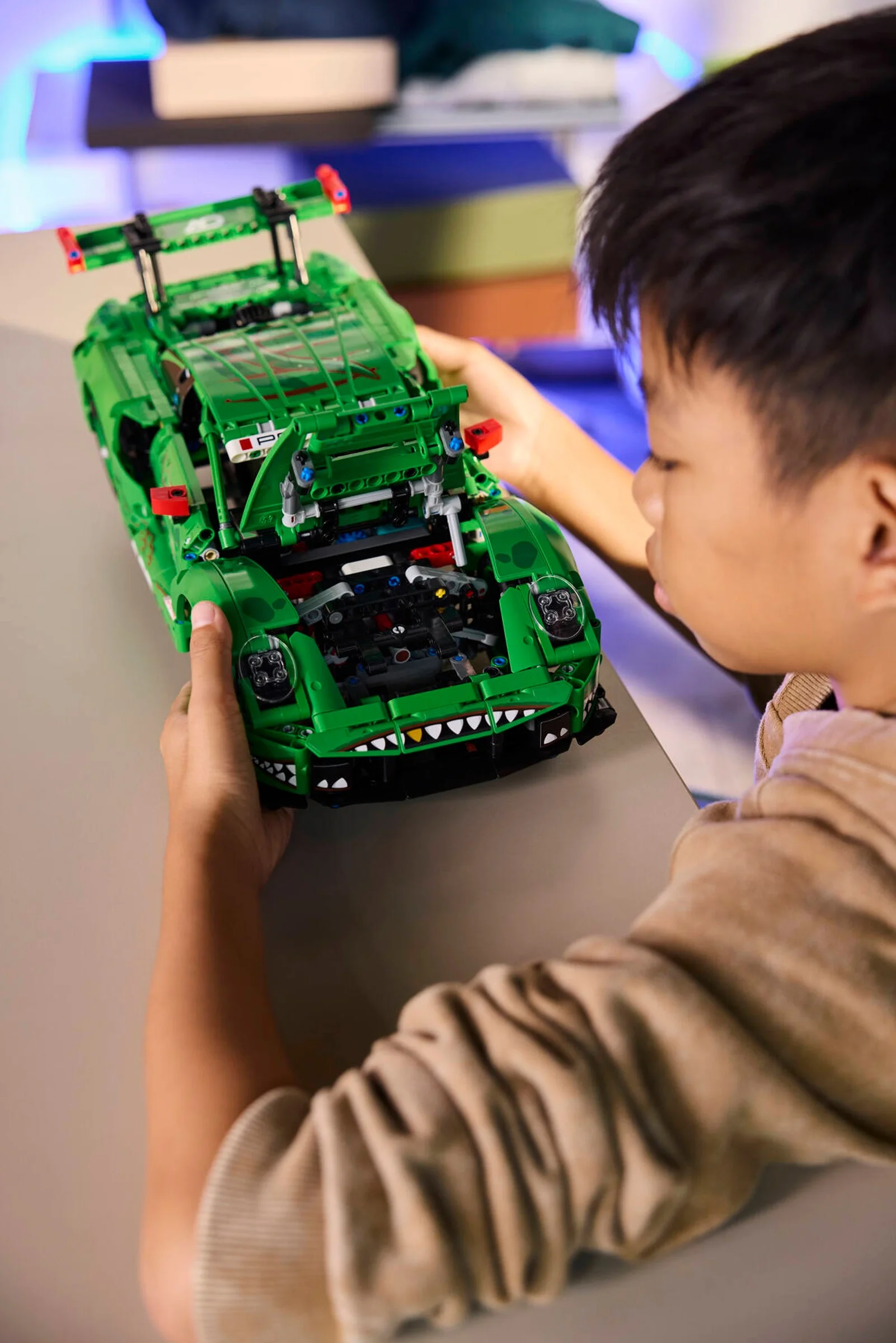 Băiat admirând Porsche 911 GT3 R REXY AO Racing, verde, construit din LEGO Technic.