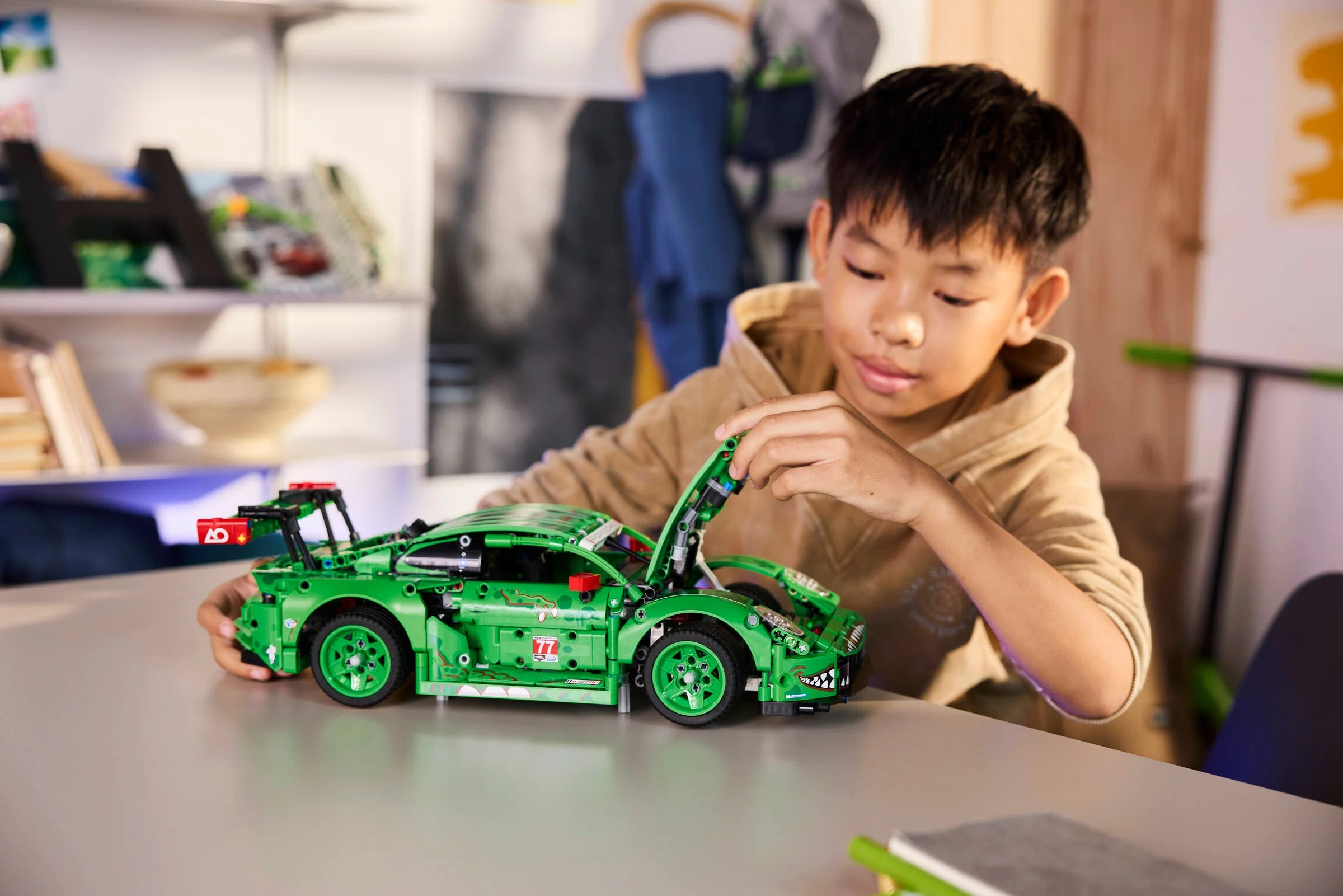 Băiat interacționând cu modelul Porsche 911 GT3 R verde, cu capota ridicată.