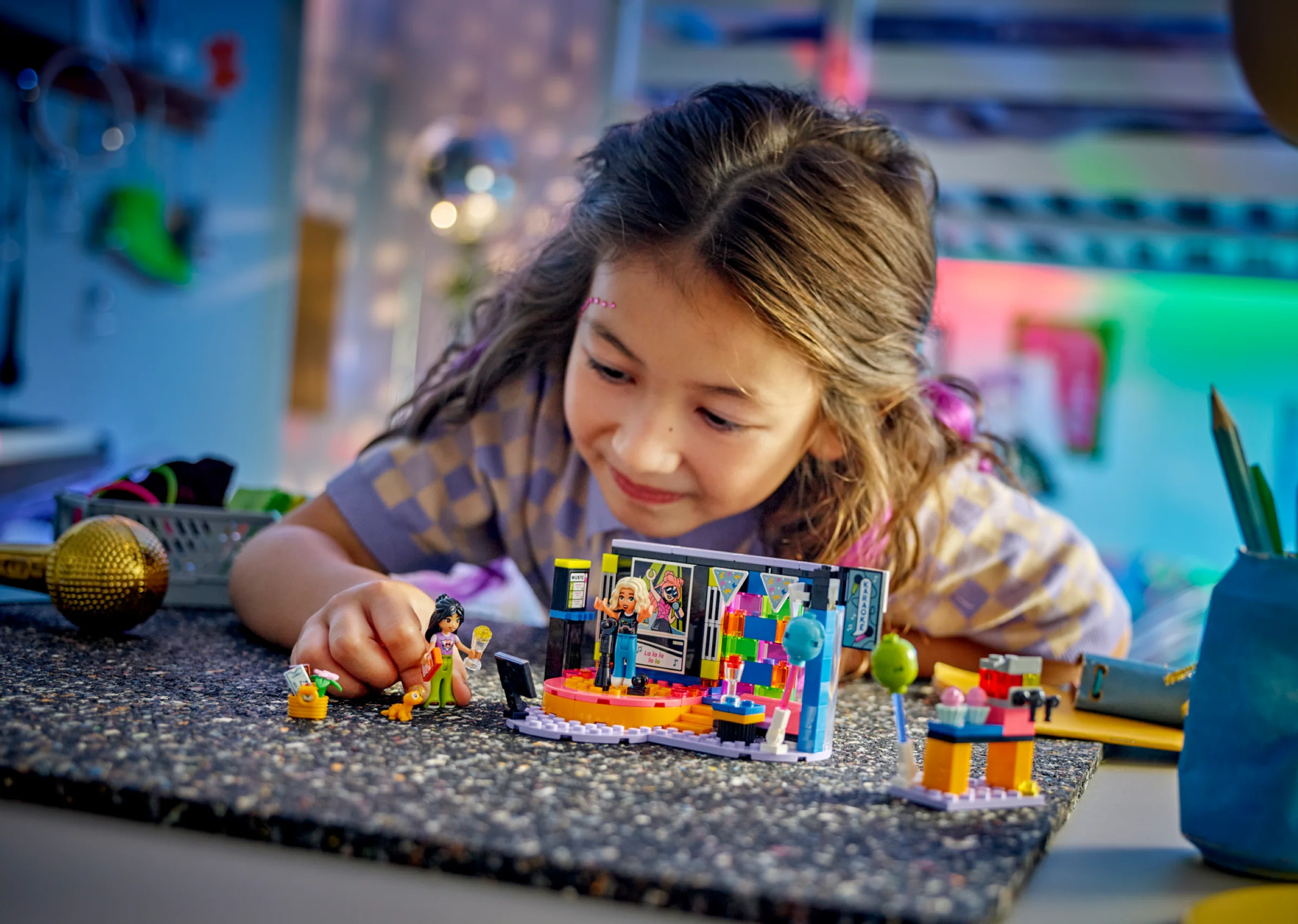 Fetiță construind setul LEGO 42610 Karaoke Music Party cu minifigurine și detalii colorate.