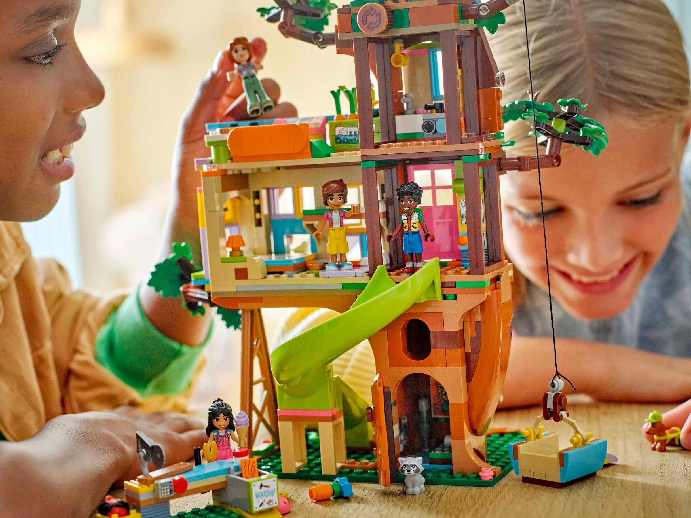 Copii se joacă cu casa din copac LEGO Friends. Setul include tobogan, atelier și funcții interactive.