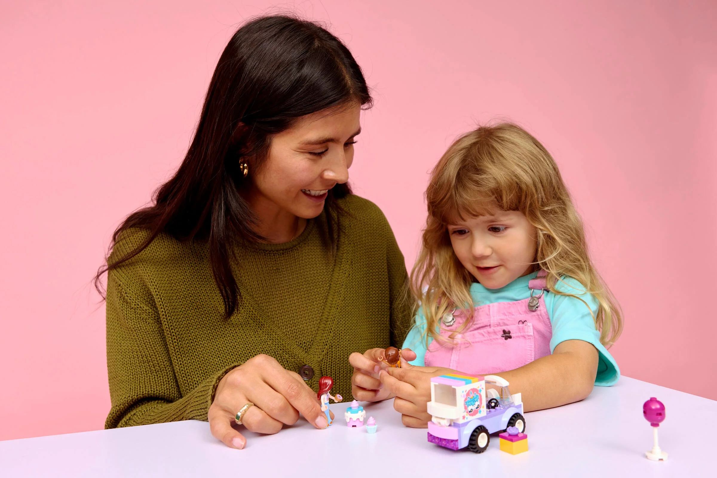 O mamă și fiica se joacă cu mașina de livrare prăjituri unicorn LEGO Friends. Imagine prietenoasă.