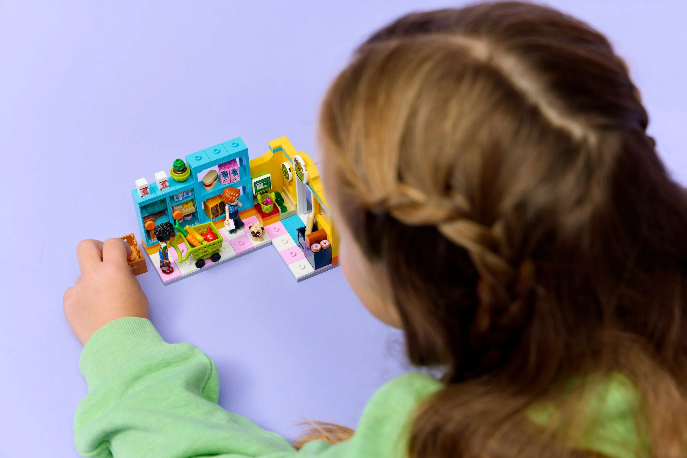 O fetiță se joacă cu setul LEGO Heartlake City Mini Supermarket. Setul are rafturi pline cu produse.