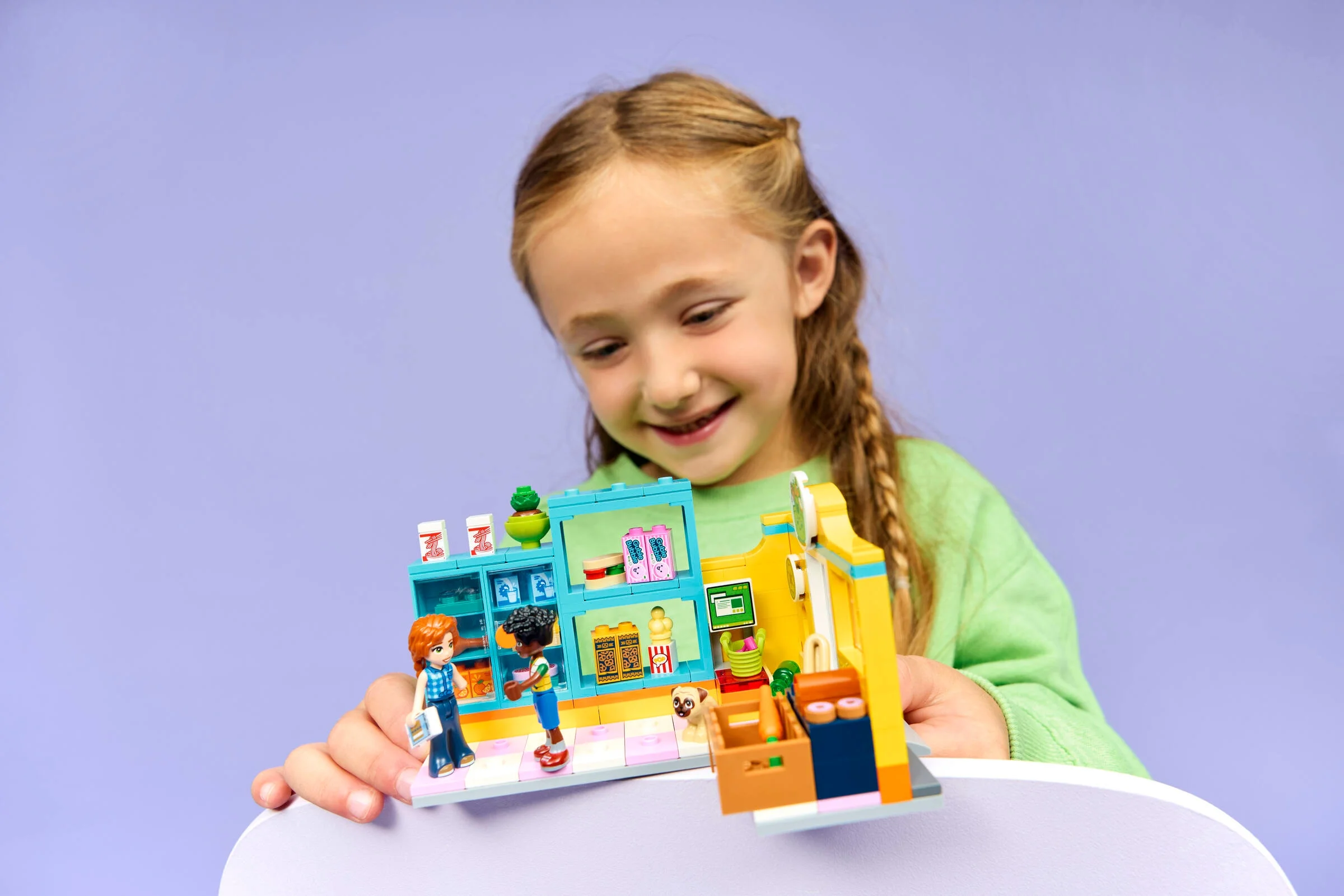 Fetiță zâmbind, ținând în mână mini supermarketul LEGO Friends Heartlake City.