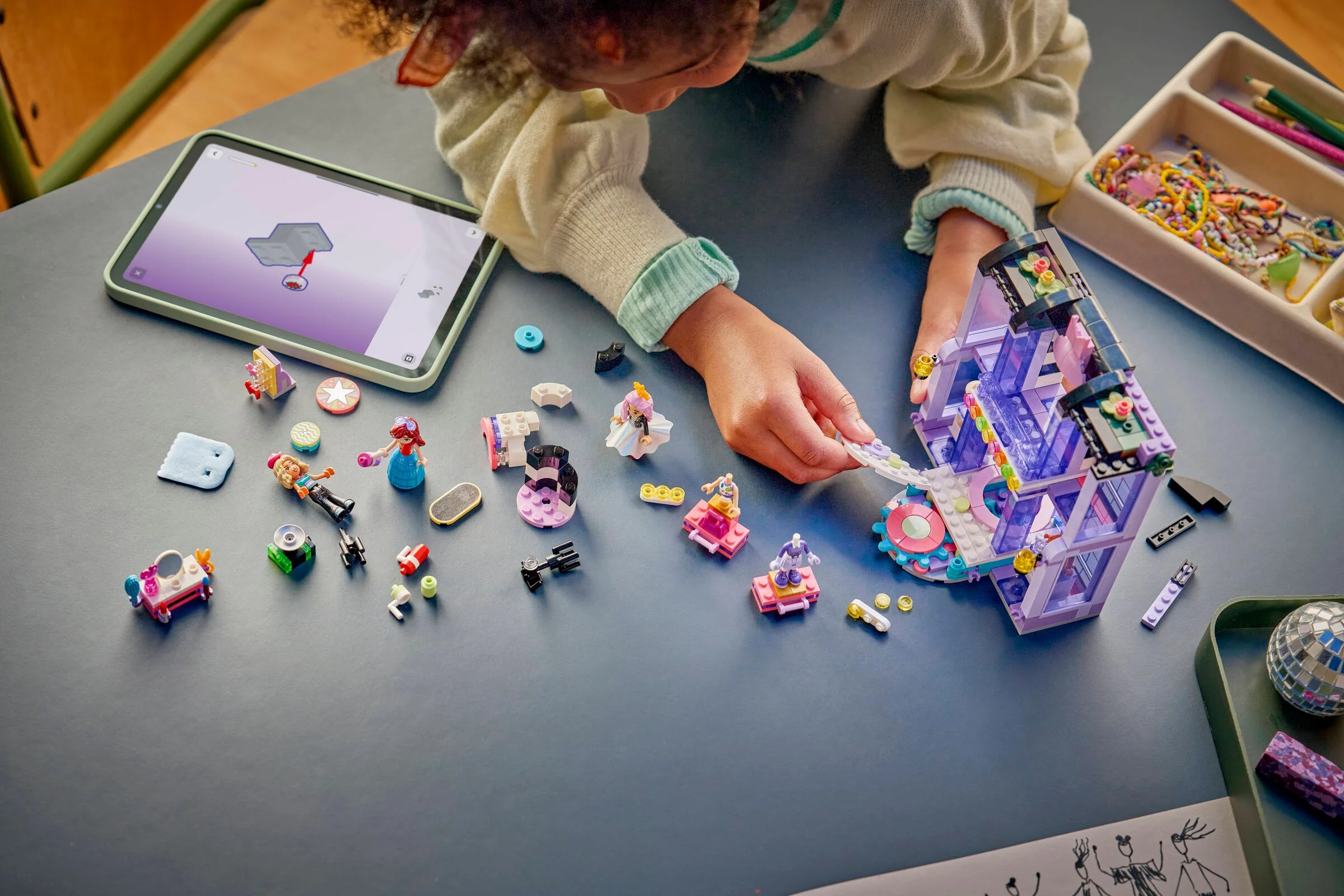 Copil construind scena de modă LEGO. Instrucțiuni digitale pe tabletă. O mulțime de piese colorate.