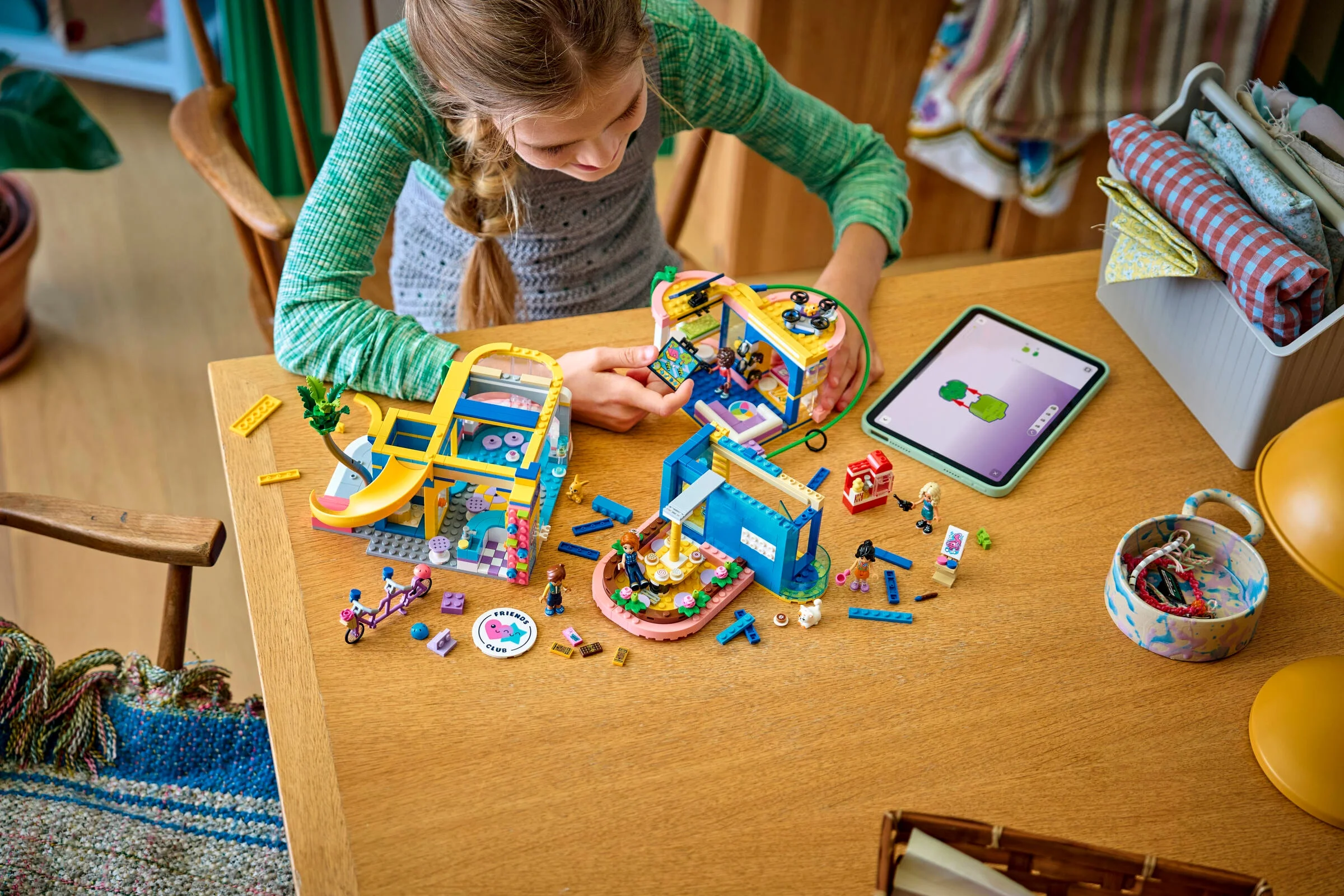 Fetiță construind Clubul Prietenilor Heartlake City LEGO 42689 folosind o tabletă cu instrucțiuni.