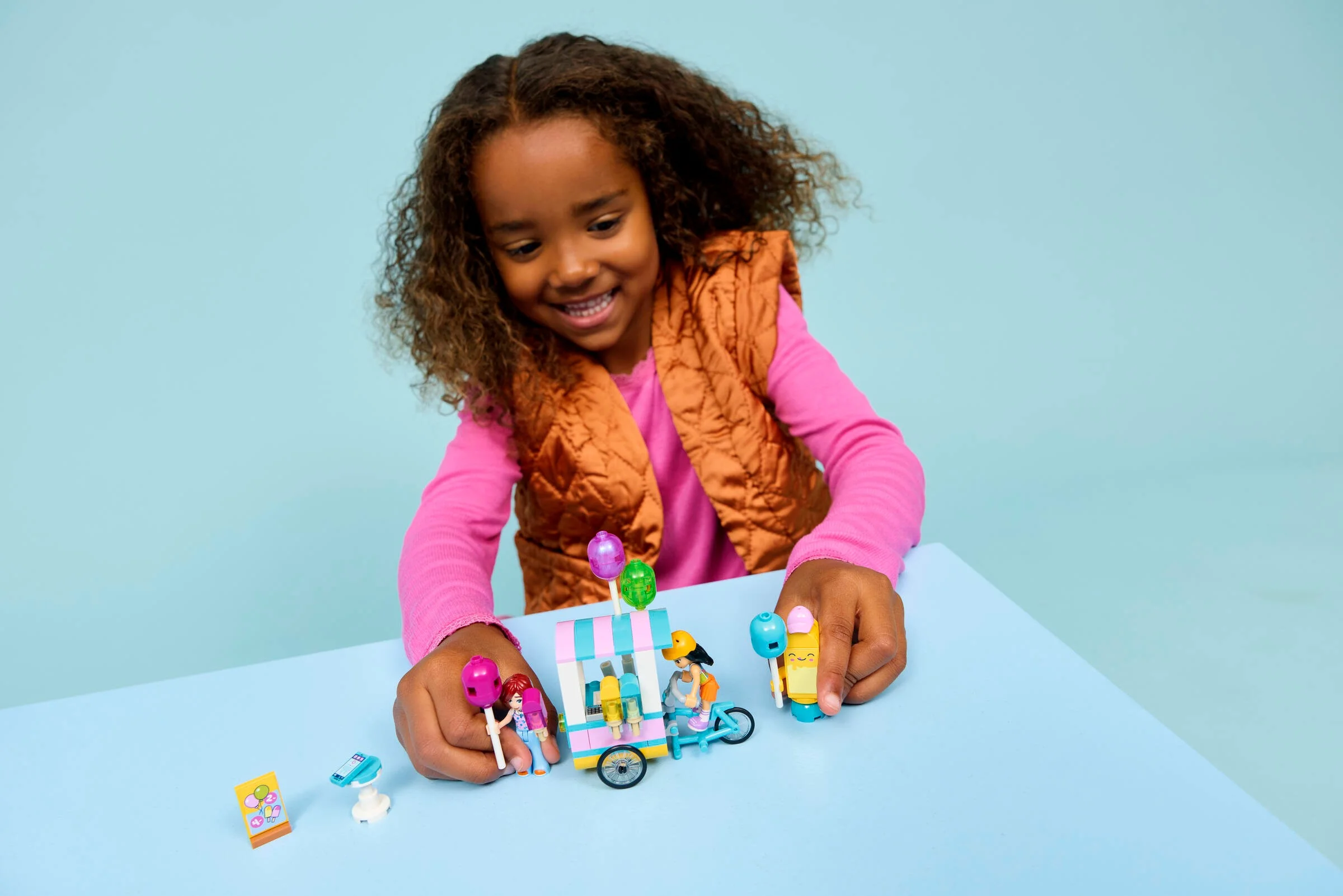 Copil fericit se joacă cu setul LEGO Friends 42692, stand de înghețată și baloane.