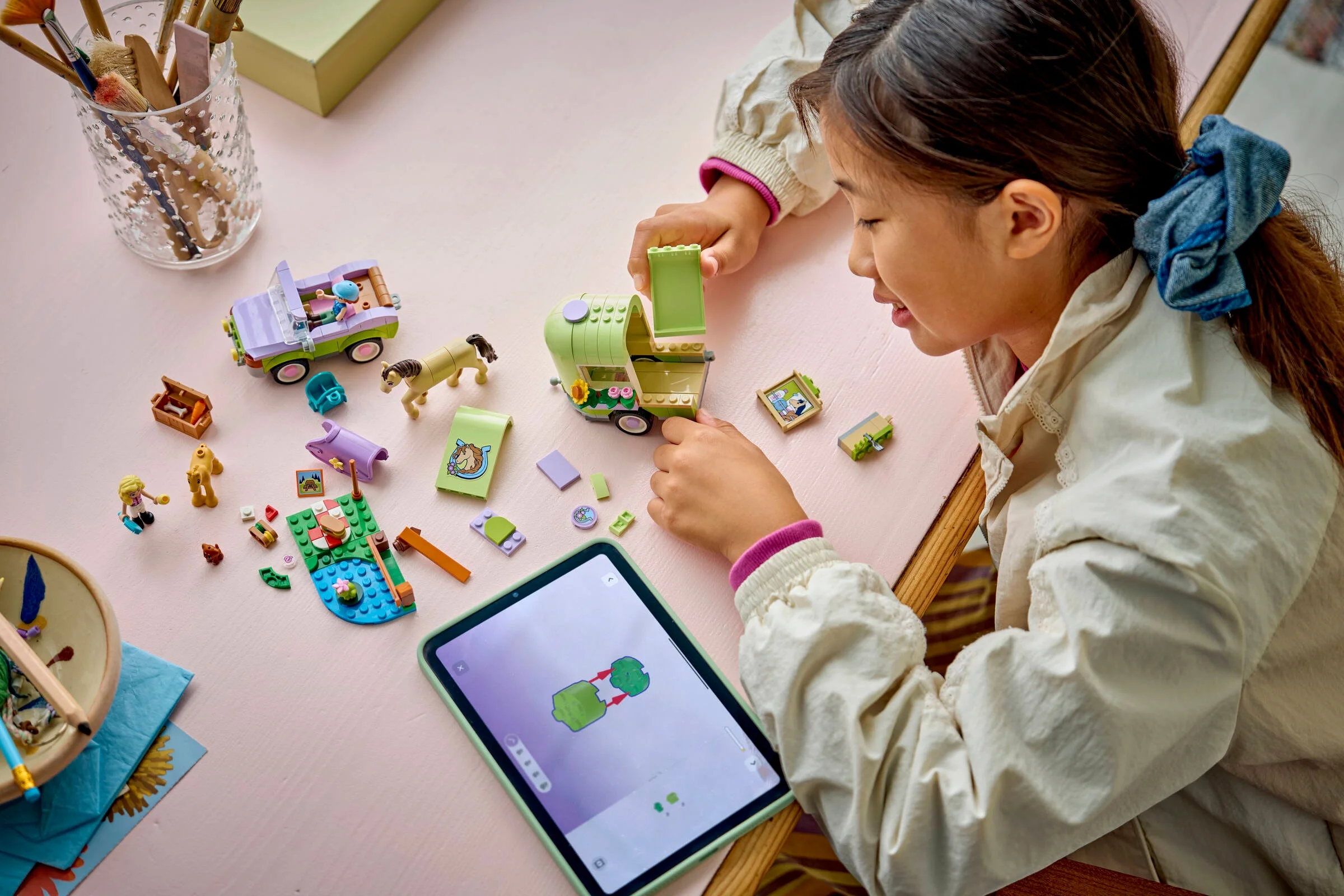 O fetiță construiește remorca de cai LEGO Friends, urmând instrucțiunile pe o tabletă.