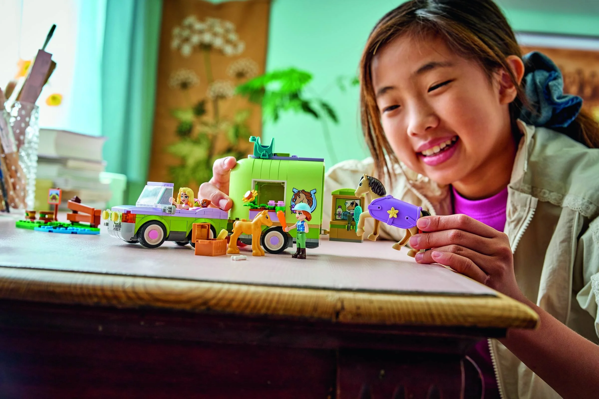 O fetiță zâmbitoare se joacă cu setul LEGO Friends Remorcă pentru Cai și Mânz (42695).