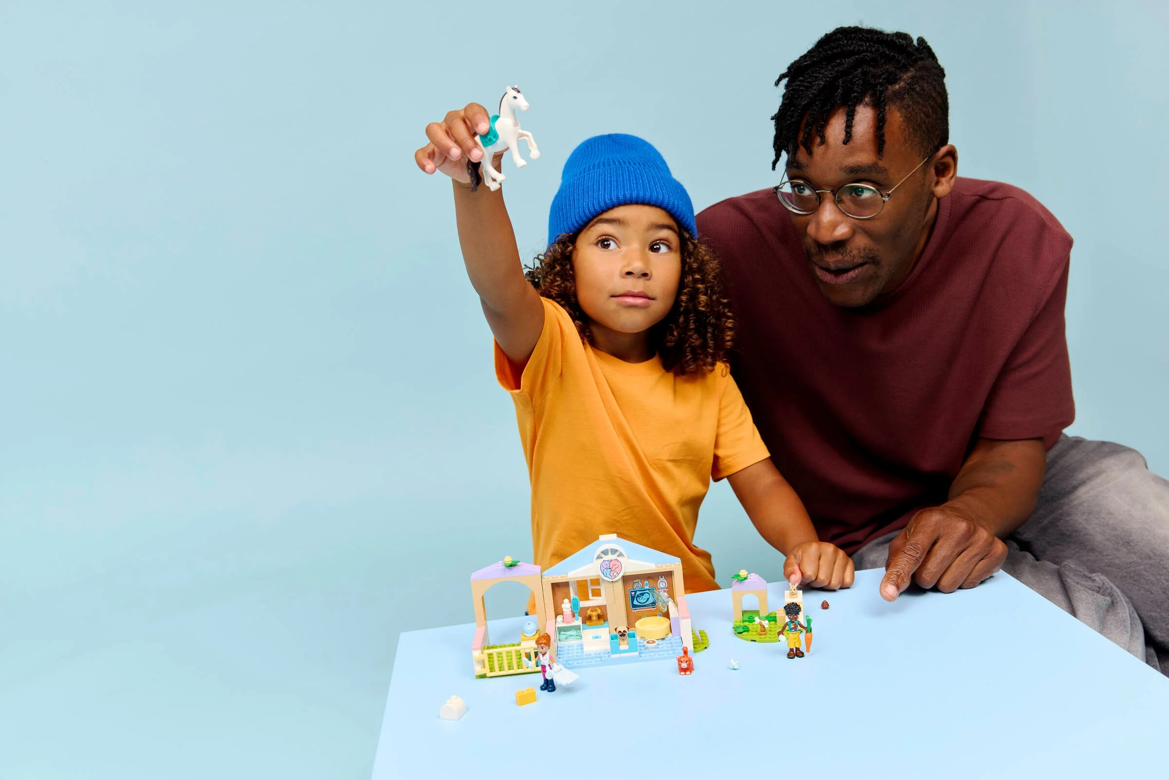 Un copil se joacă cu setul LEGO Friends 42696 Clinica veterinară, asistat de tatăl său.