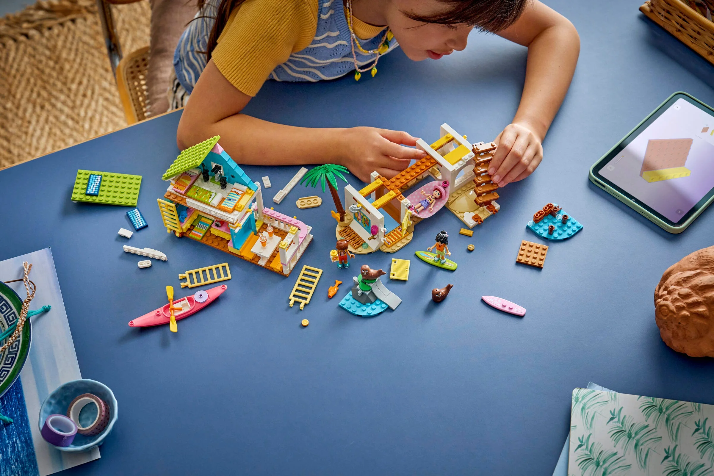 O fetiță construiește setul LEGO 42699, Casa de pe Plajă cu Foci, urmând instrucțiunile de pe o tabletă.
