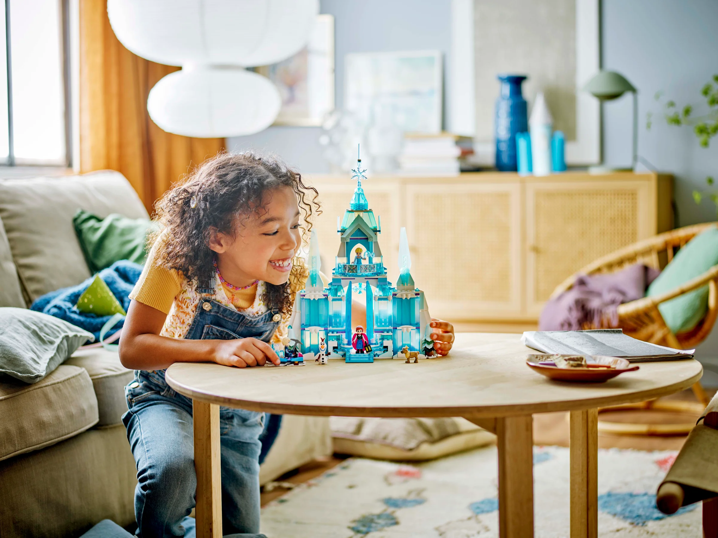 O fetiță se joacă cu Palatul de Gheață al Elsei, un set LEGO Disney. Zâmbet larg, bucurie.