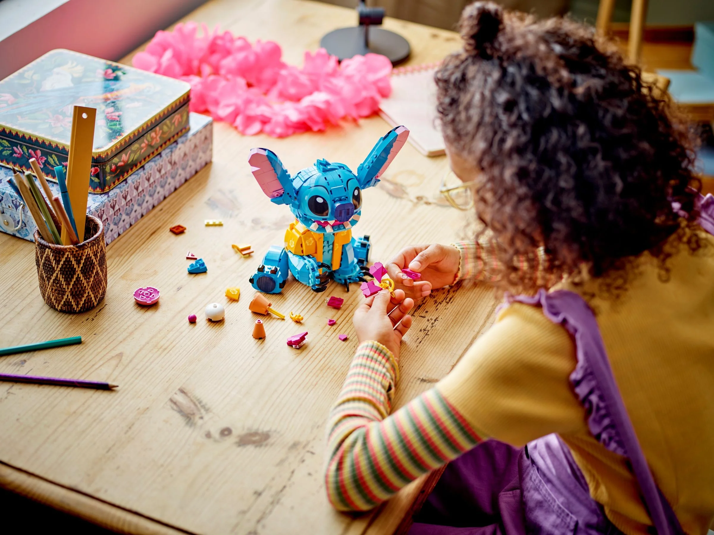 O fetiță construiește modelul LEGO Stitch, folosind diverse piese colorate.