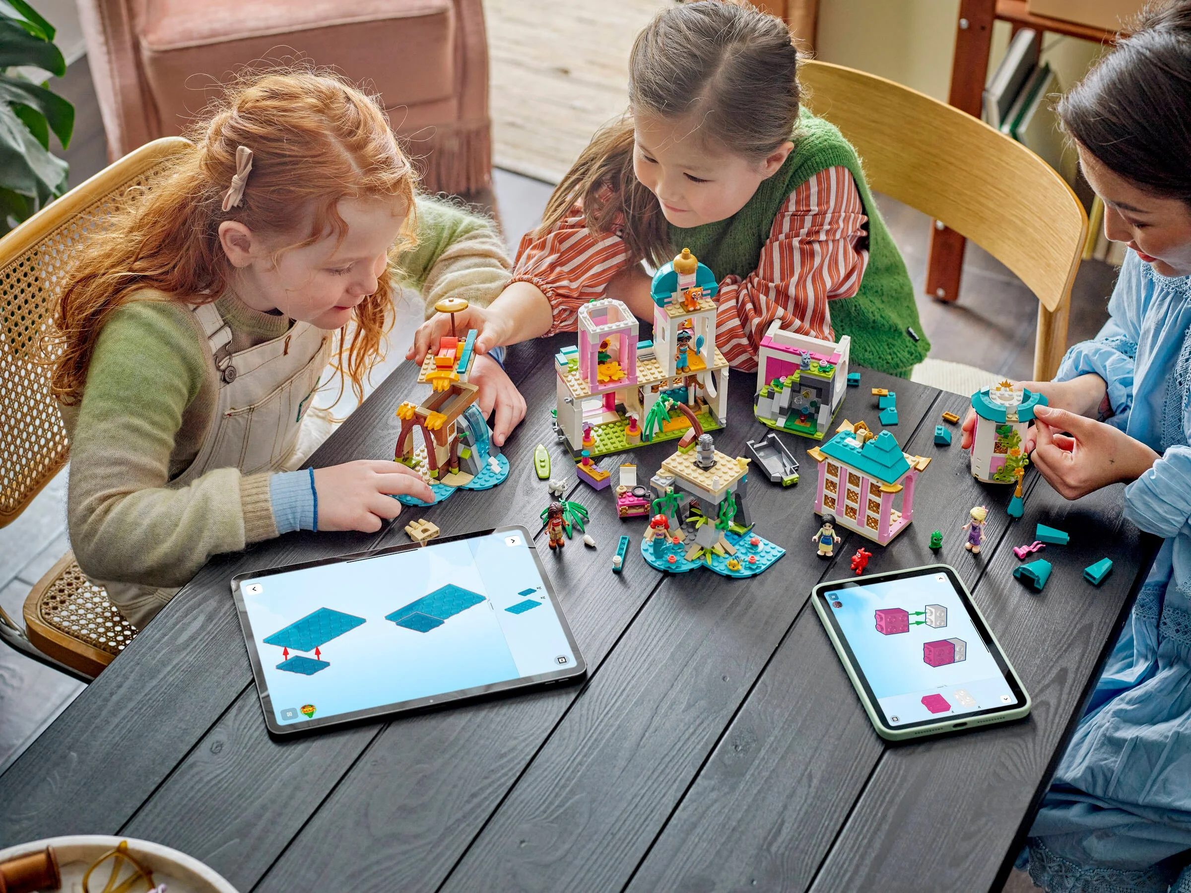 Trei copii construiesc castelul prințeselor Disney cu ajutorul instrucțiunilor digitale pe tabletă.
