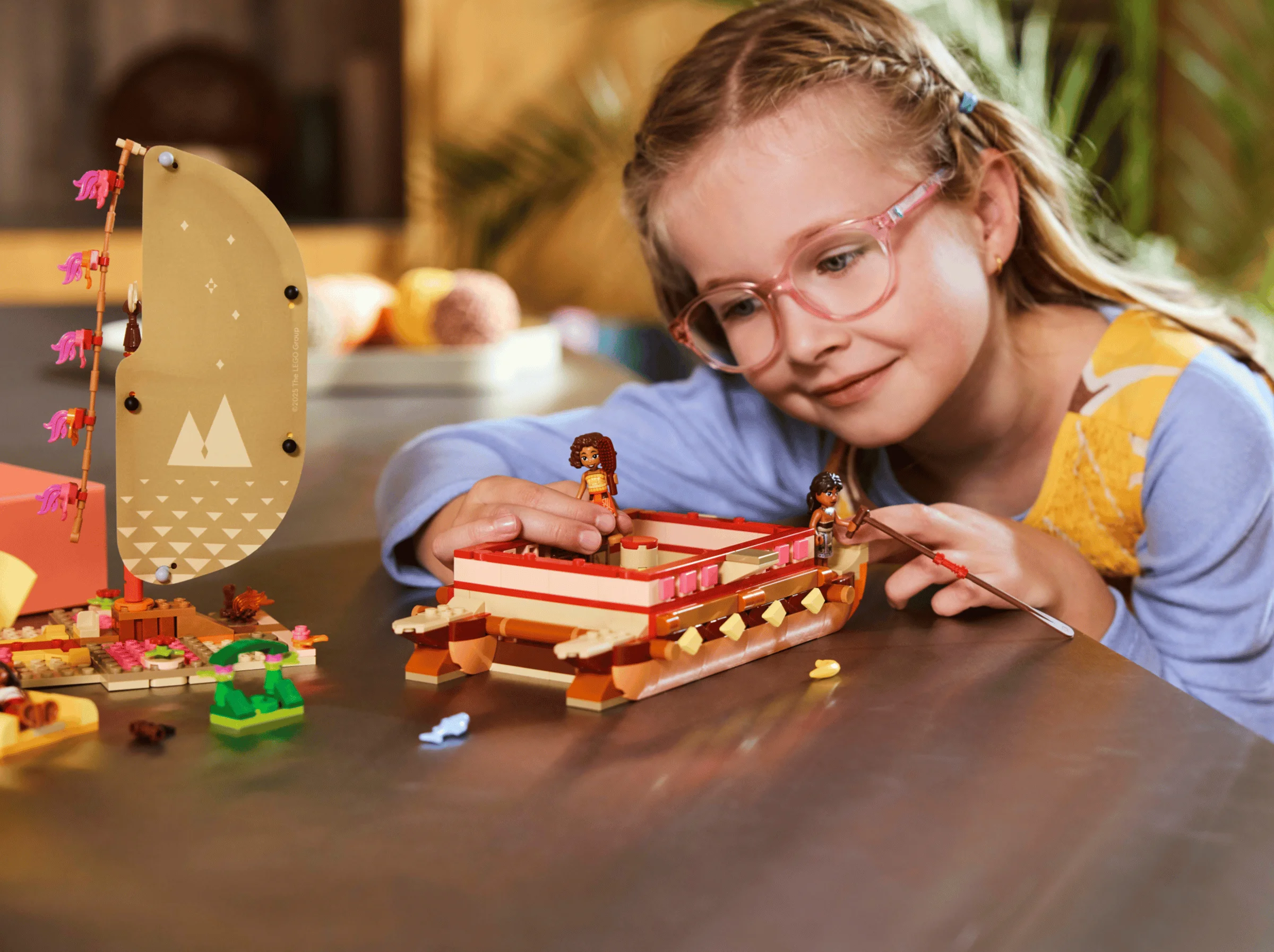 O fetiță se joacă cu setul LEGO Moana, canoea și minifigurinele, într-o scenă plină de bucurie.