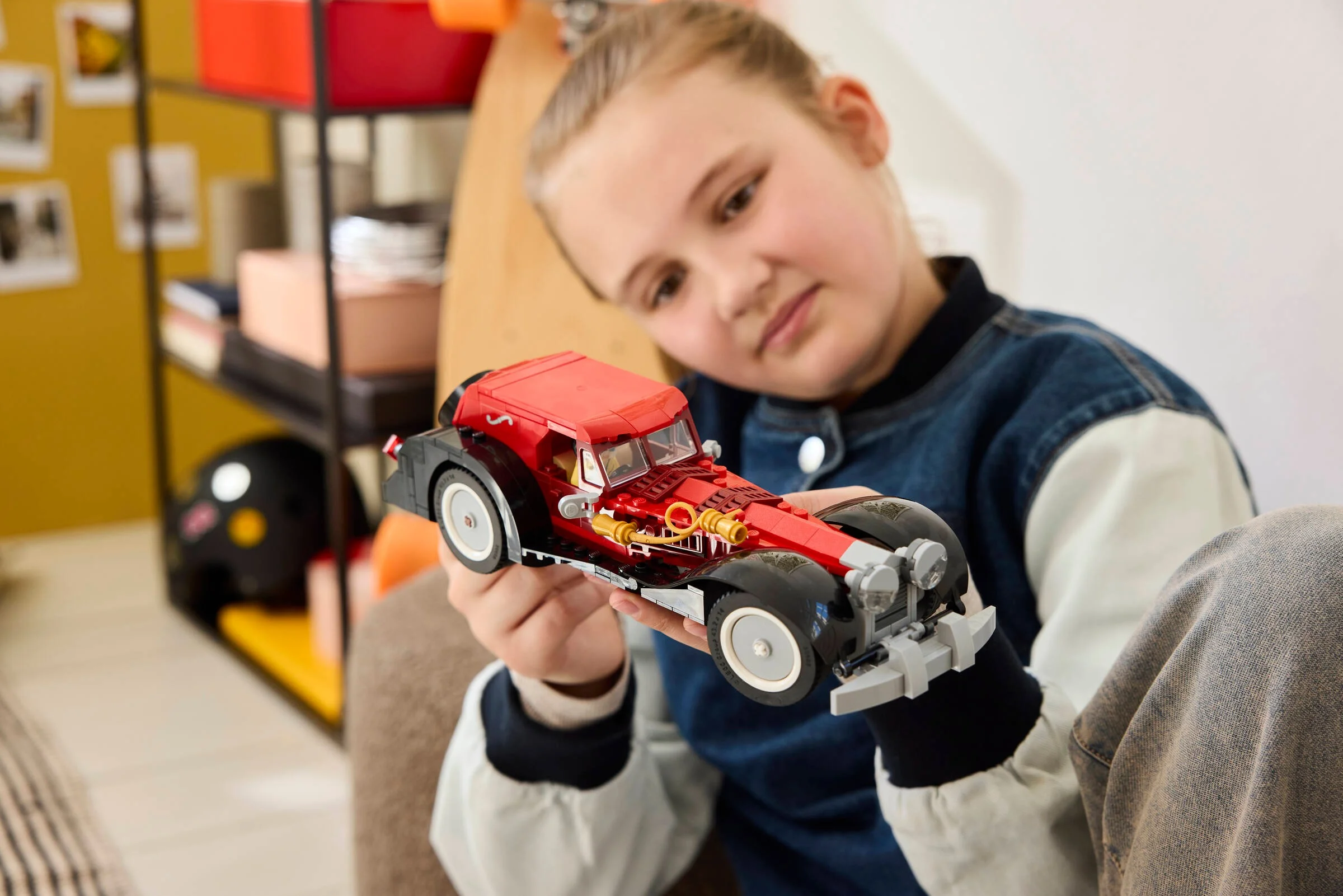 O fată admiră mașina Cruellei De Vil, un model LEGO detaliat, roșu și negru.