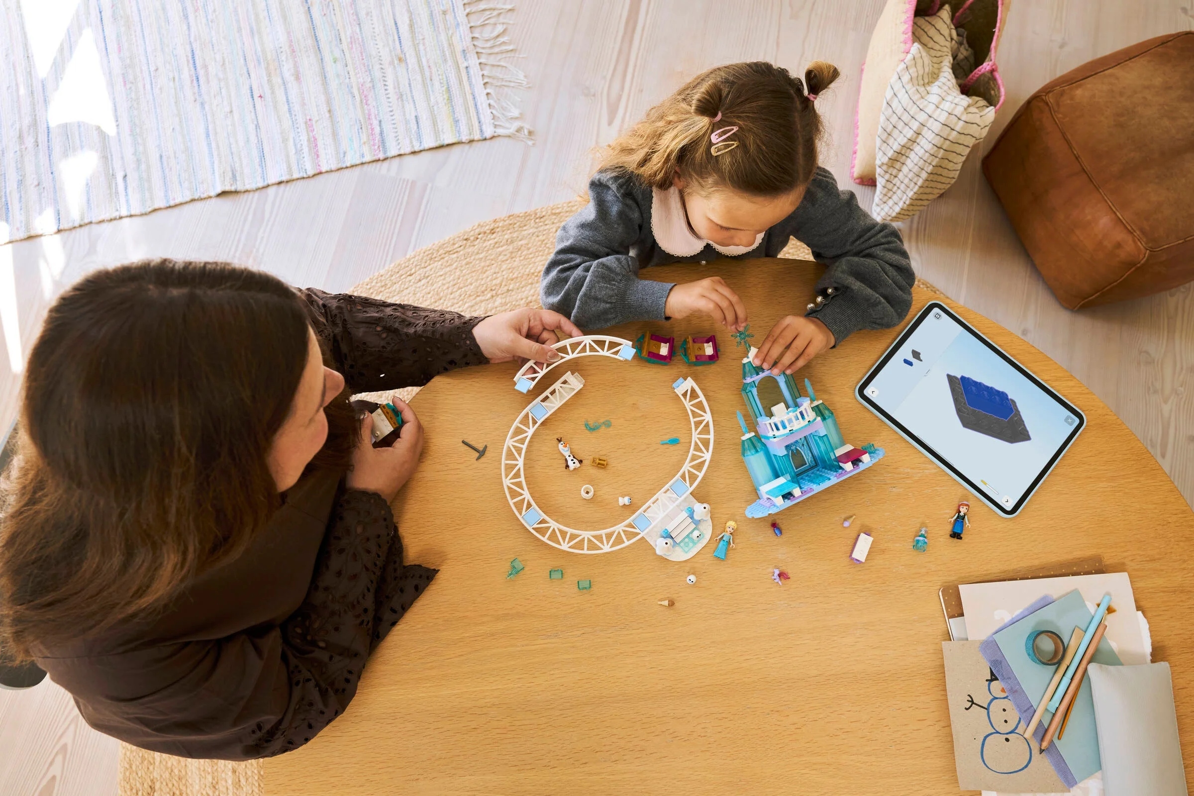 Mamă și fiică asamblând setul LEGO Elsa's Ice Castle, urmând instrucțiunile de pe tabletă.
