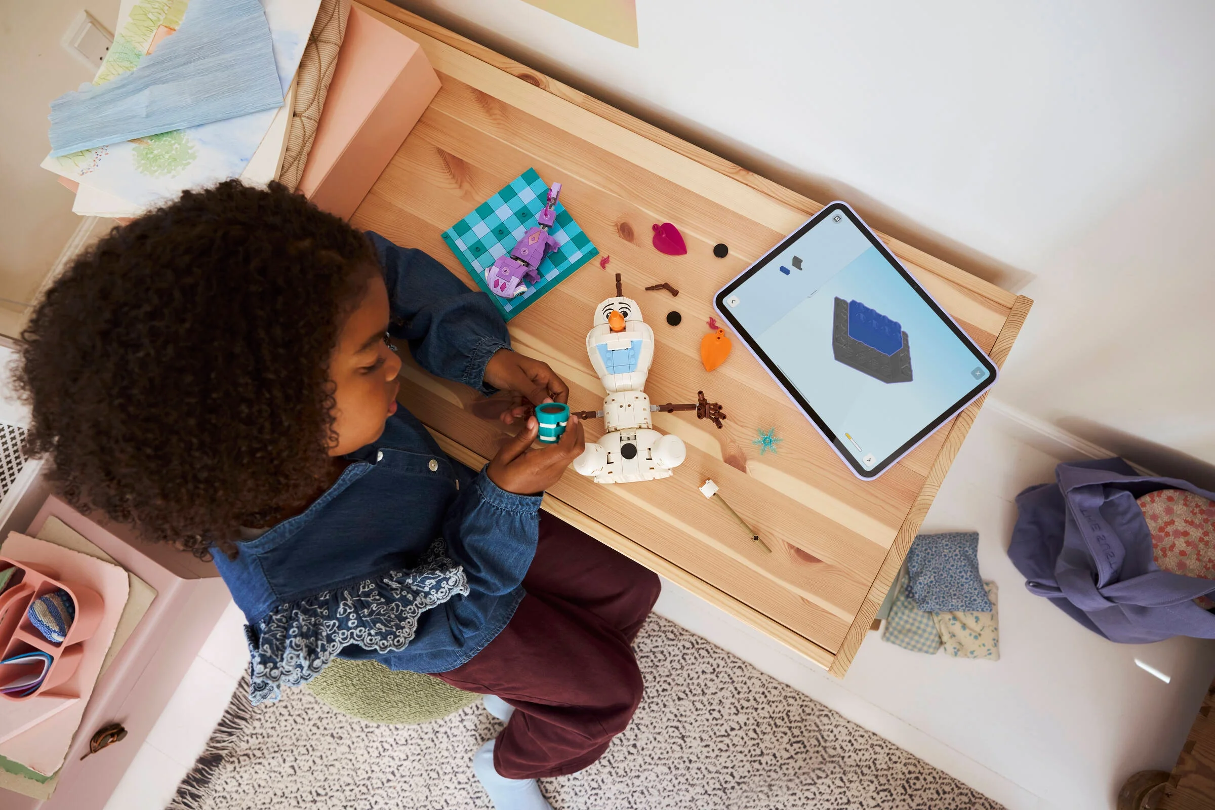 Copil construind setul LEGO Olaf și Bruni la o masă, urmând instrucțiunile de pe o tabletă.