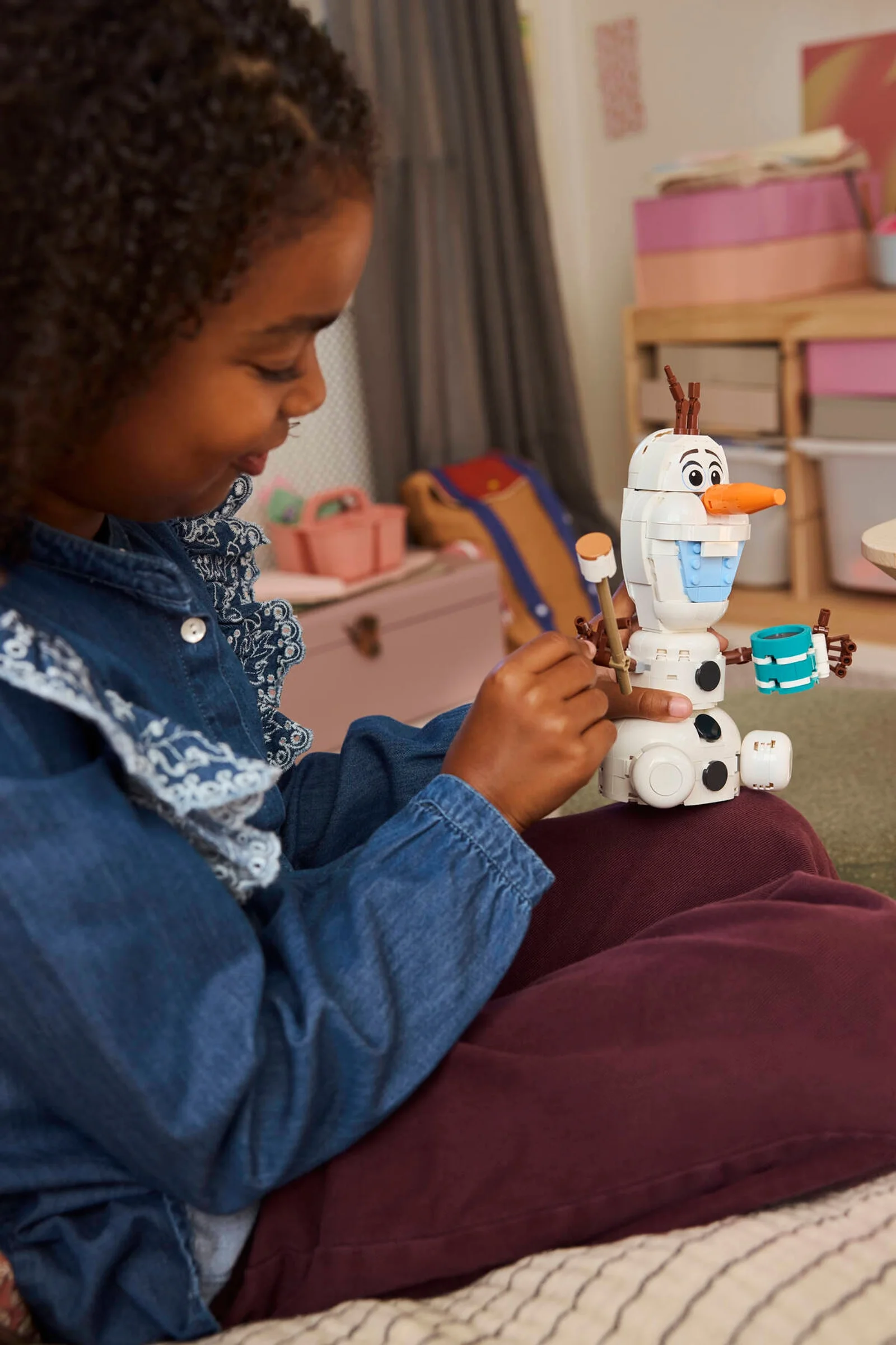 Fetiță zâmbitoare se joacă cu Olaf LEGO. Set Disney pentru distracție creativă.