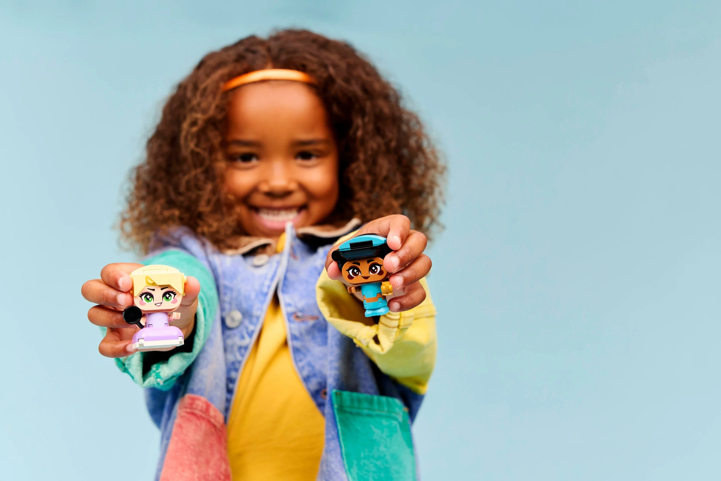 O fetiță zâmbitoare prezintă mini-figurinele LEGO Jasmine și Rapunzel.