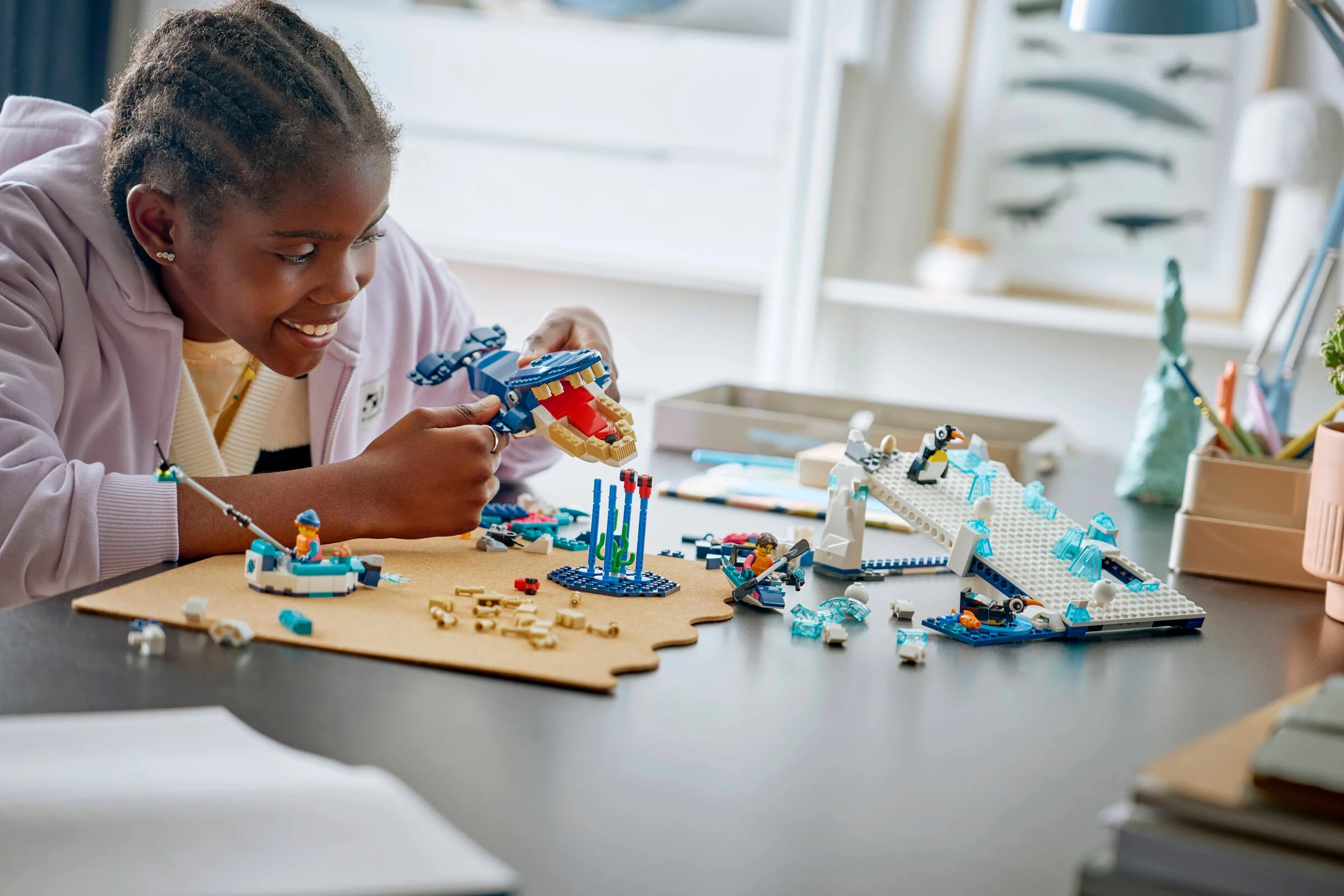 O fată zâmbind construiește un set LEGO cu animale antarctice pe un birou ordonat.
