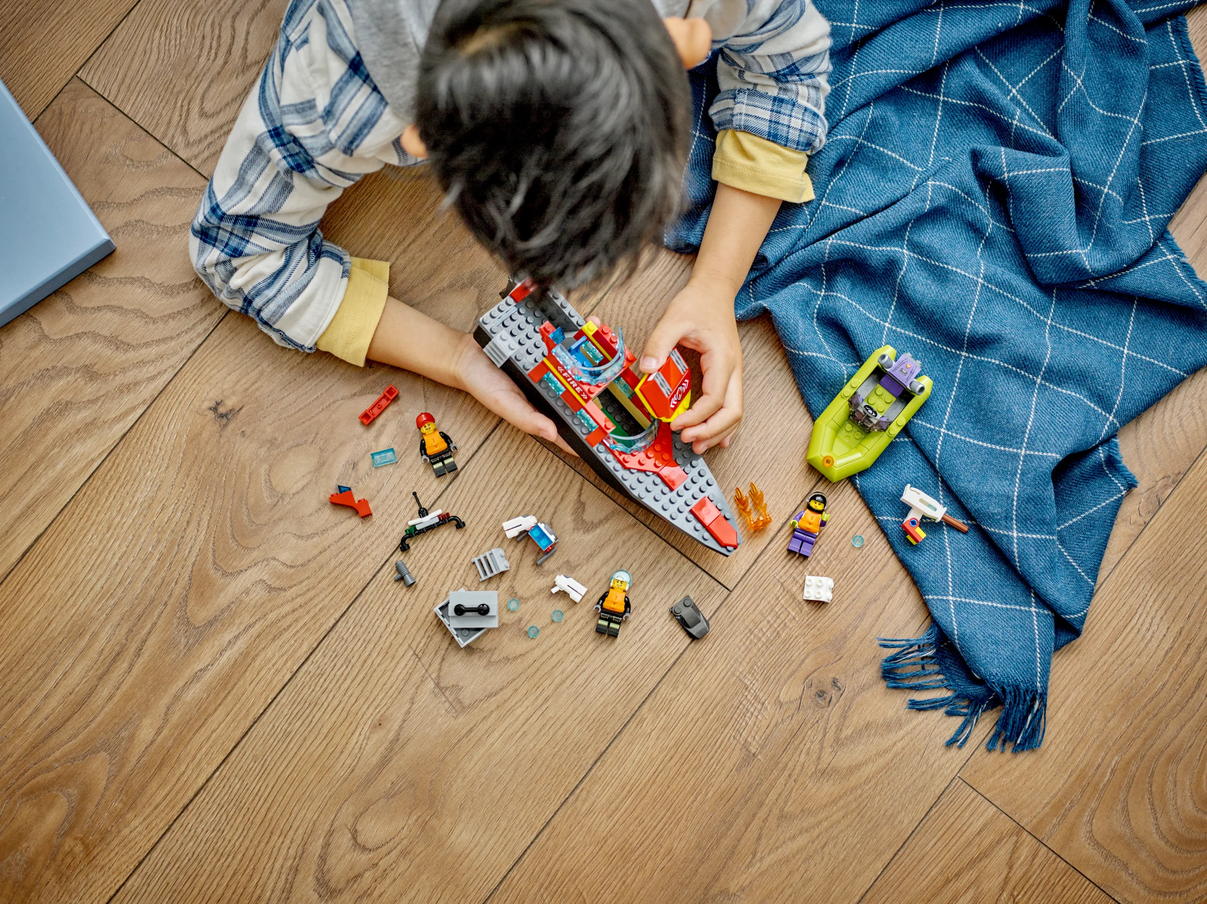 Copil se joacă cu setul LEGO 60373, asamblând barca de pompieri și alte elemente. Distracție garantată!