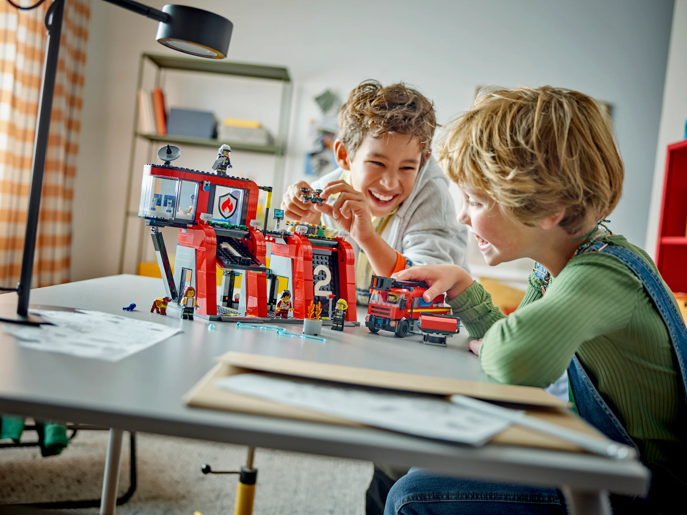 Doi copii zâmbitori se joacă cu stația de pompieri LEGO City 60414 și autospeciala.
