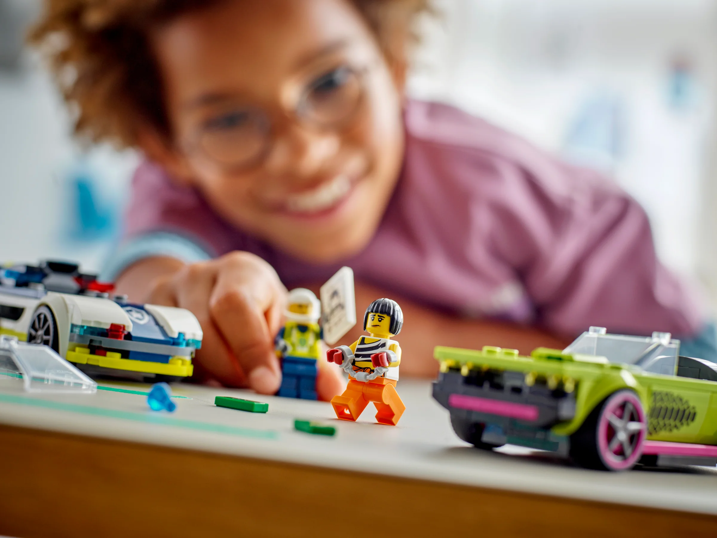 Un copil zâmbitor se joacă cu setul LEGO Poliție și Muscle Car. Mașini și minifigurine.