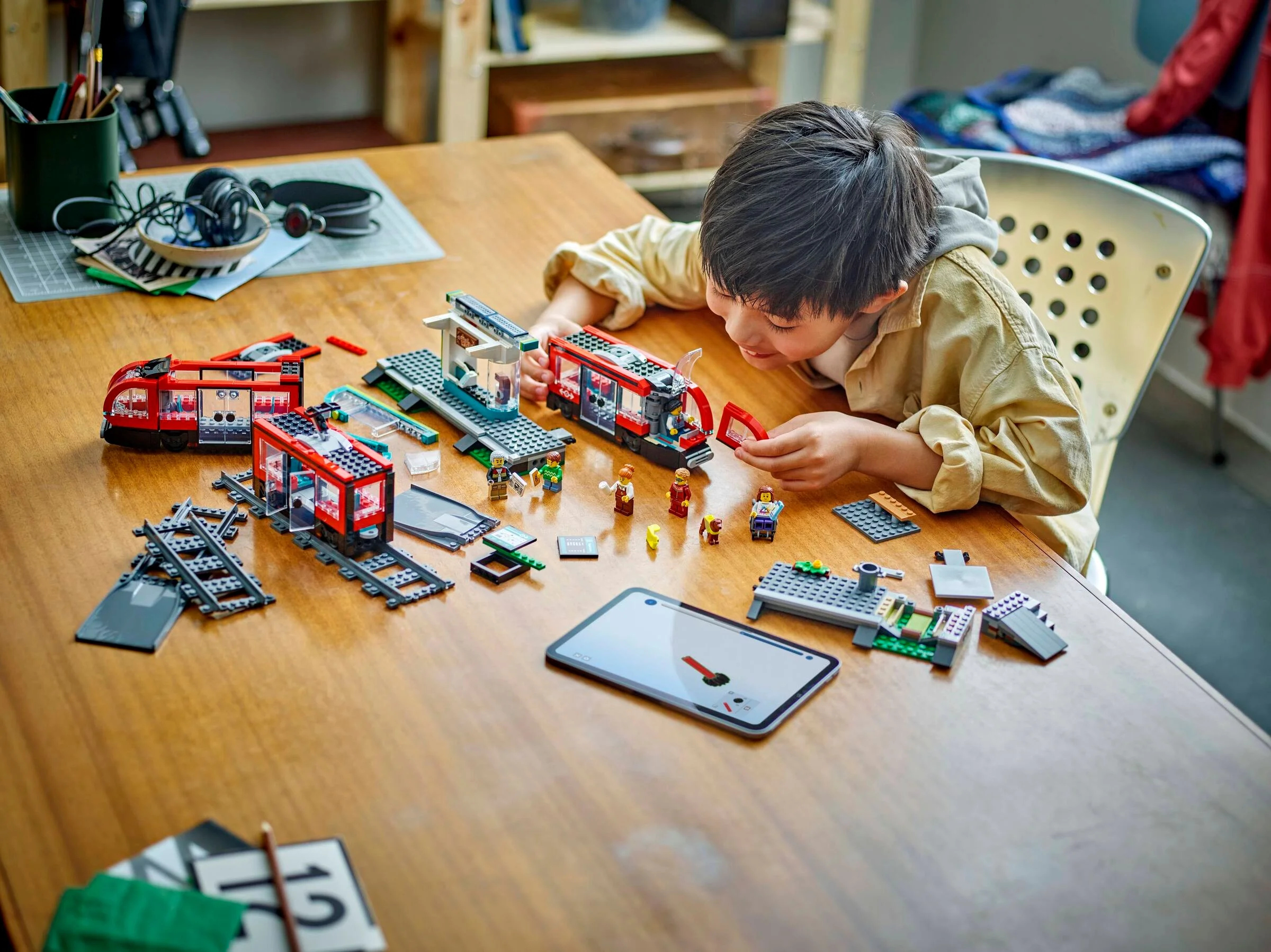 Băiat construind tramvaiul LEGO City, cu o stație și figurine. Distracție și creativitate!