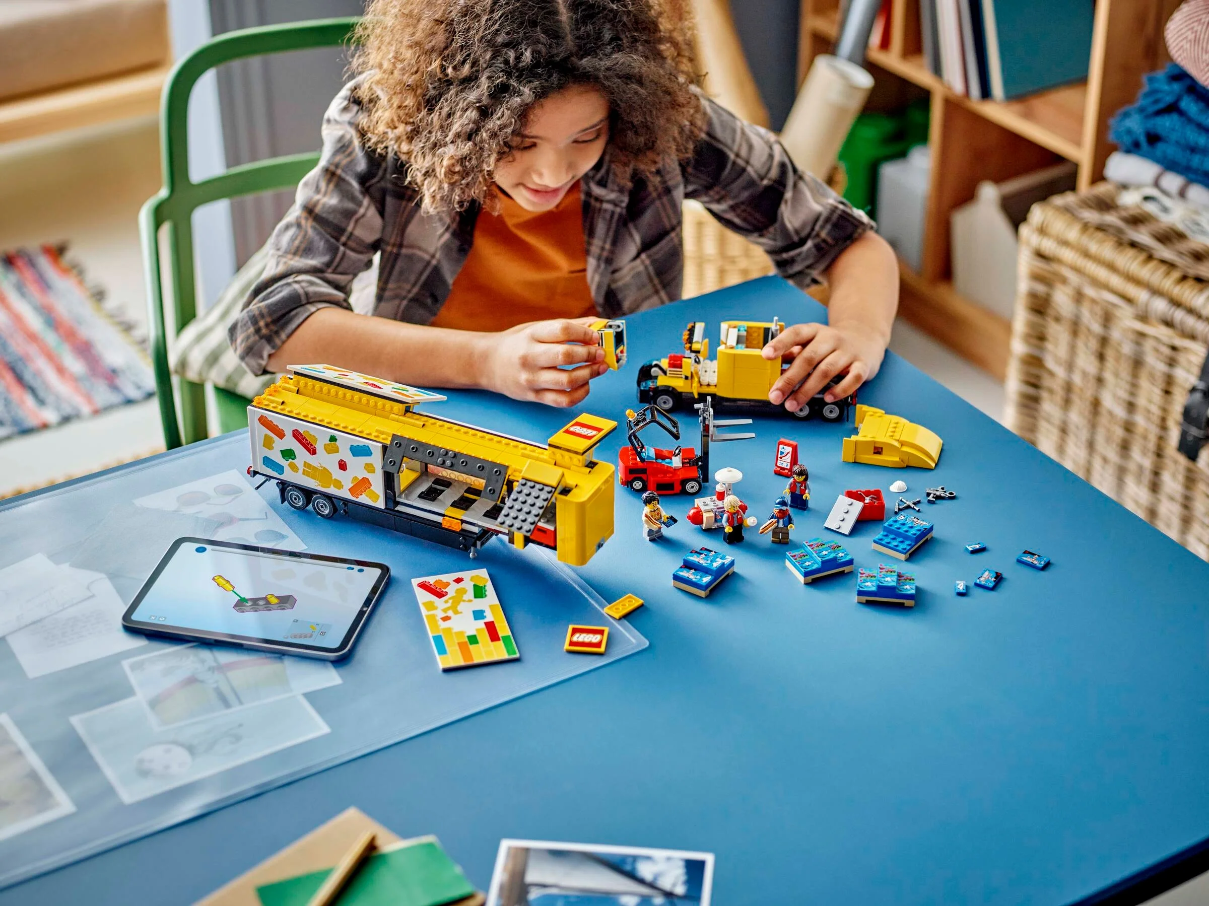 O fetiță construiește camionul de livrări LEGO, folosind instrucțiuni digitale pe tabletă.