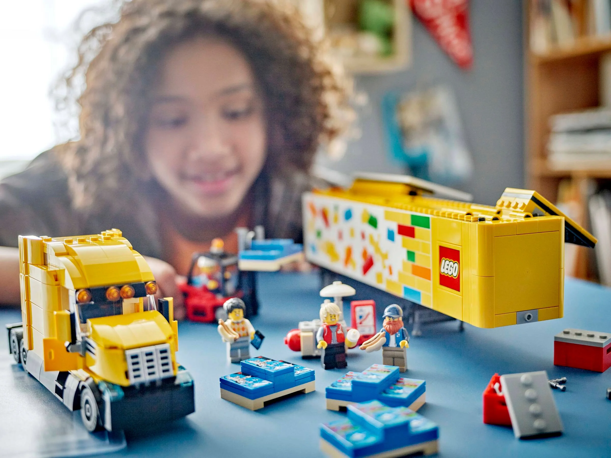 Fetiță zâmbitoare se joacă cu camionul LEGO și minifigurinele acestuia. Distracție garantată!