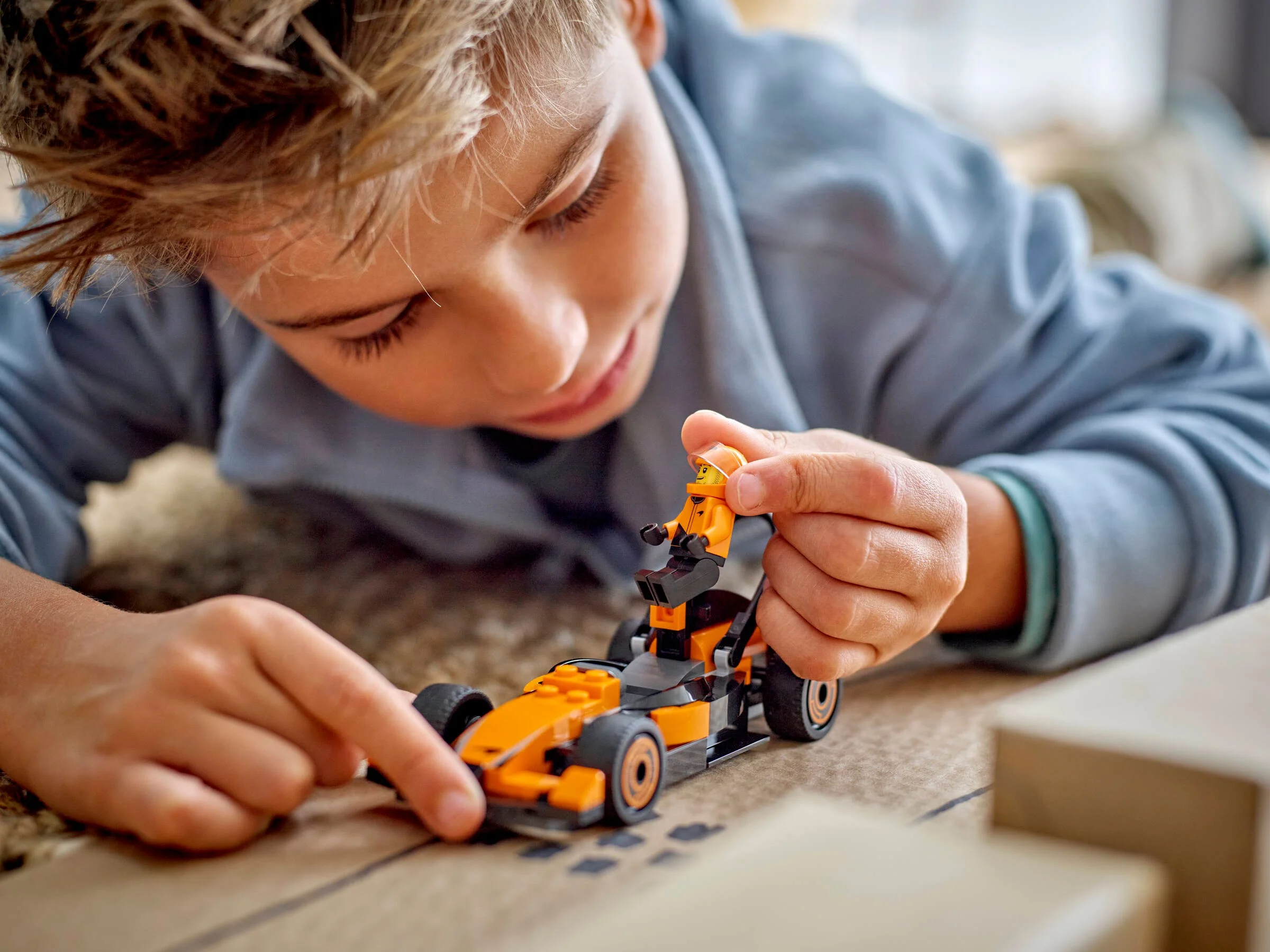 Un copil se joacă cu mașina de curse McLaren LEGO, așezând șoferul înăuntru.