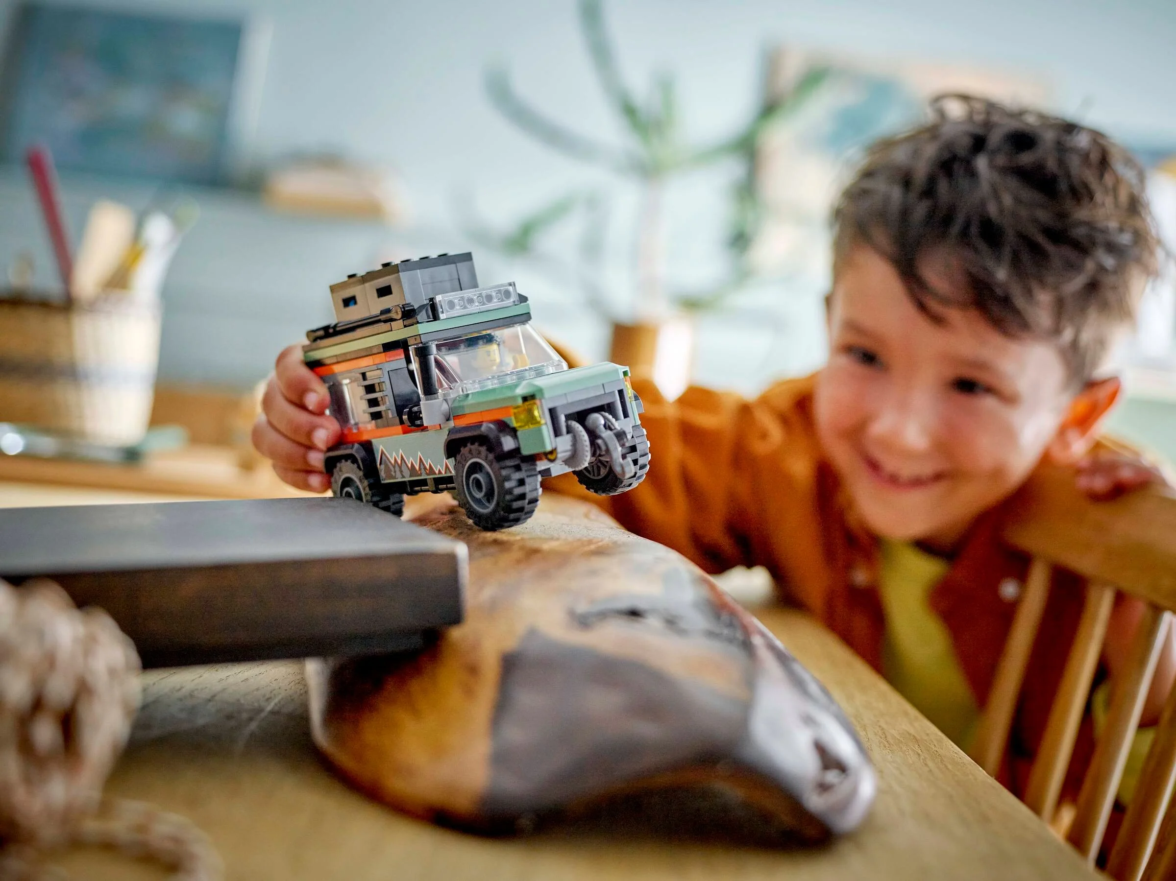 Băiat zâmbitor ținând în mână camionul off-road LEGO 60447, explorând. O imagine plină de bucurie.