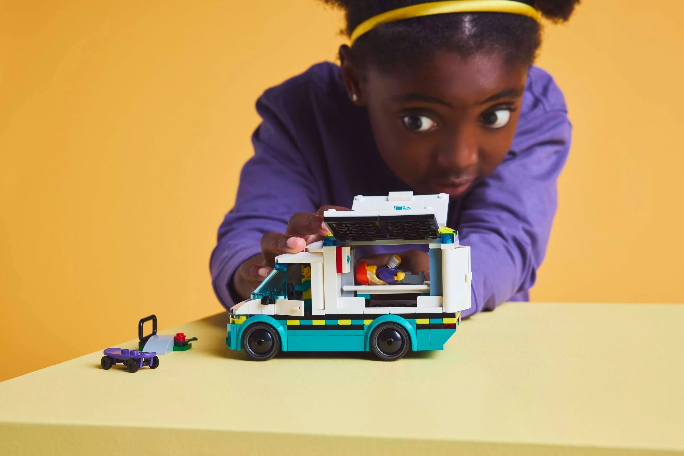 Fetiță interacționând cu Ambulanța LEGO City. Acoperiș deschis, targă vizibilă.