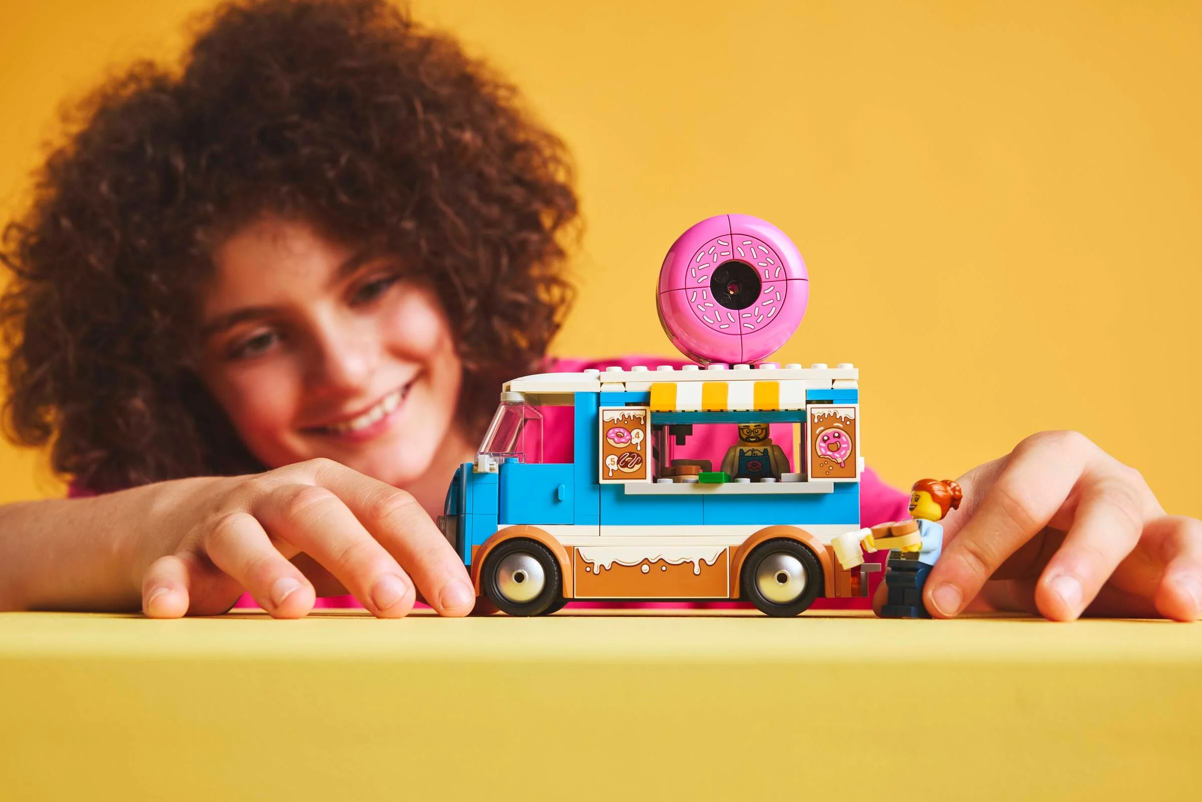 Camionul de gogoși LEGO City 60452. O fată se joacă cu setul pe un fundal galben.