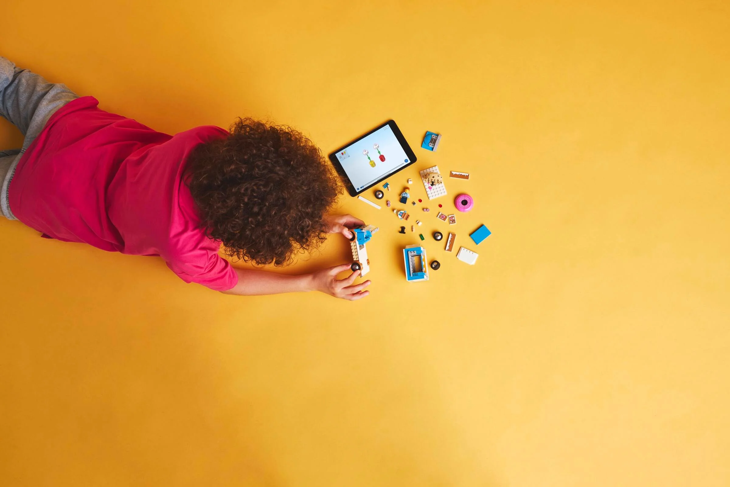 Copil construind camionul de gogoși LEGO City, urmând instrucțiuni pe tabletă.