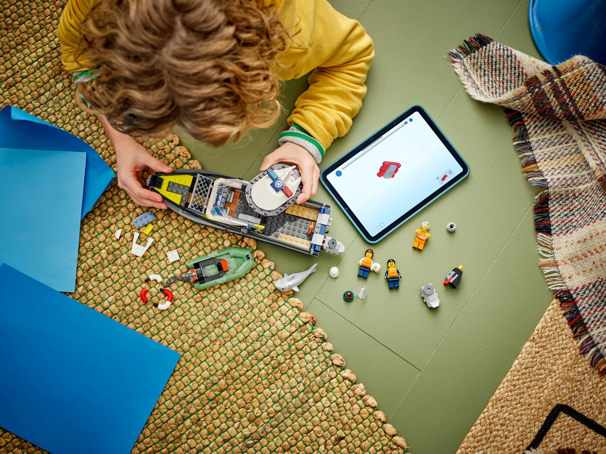 Copil asamblând setul LEGO 60456 Poliția Navală folosind instrucțiuni pe tabletă. Distracție cu jucării!