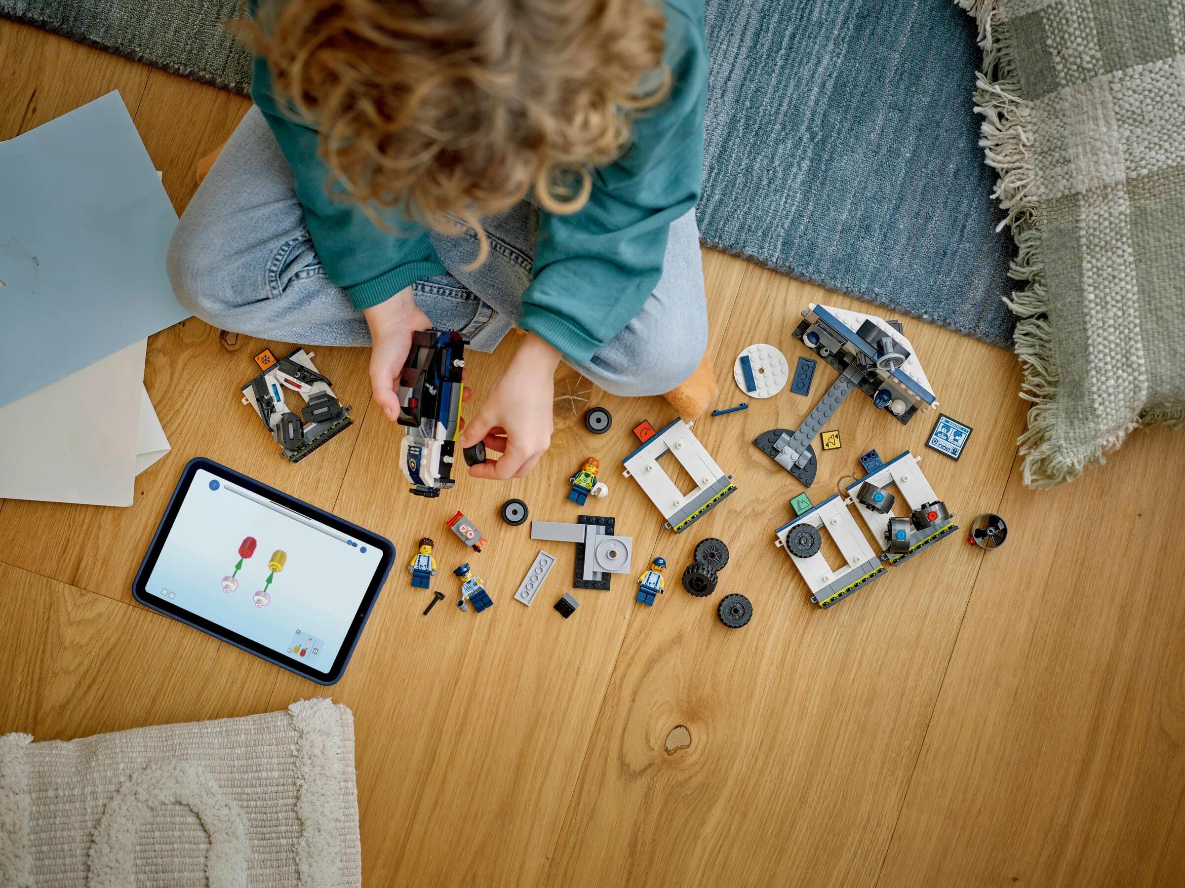 Copil asamblând setul LEGO Garaj de Poliție personalizat (60457) pe podea, folosind o tabletă cu instrucțiuni.