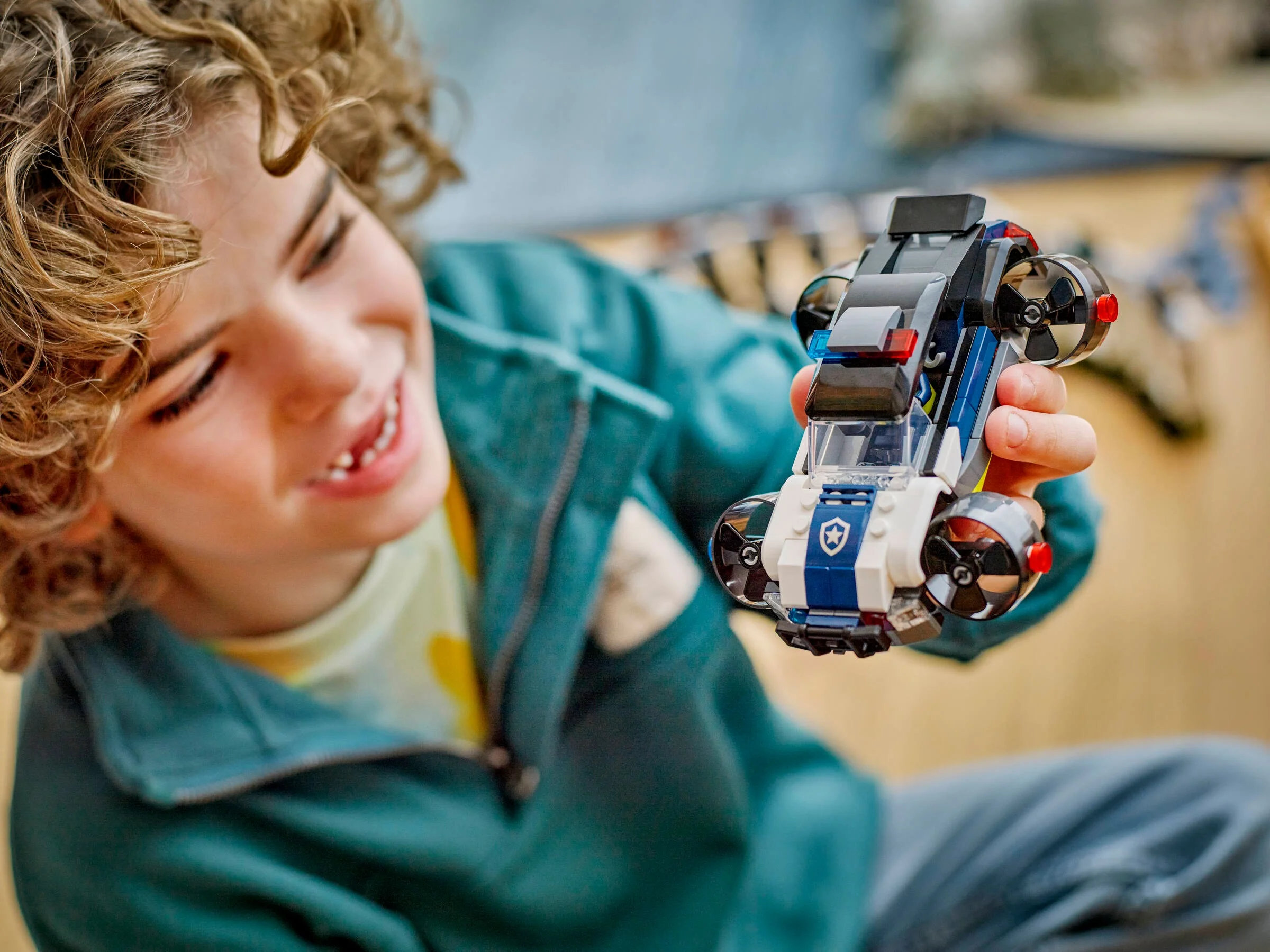Copil zâmbitor ținând o mașină de poliție zburătoare LEGO City.