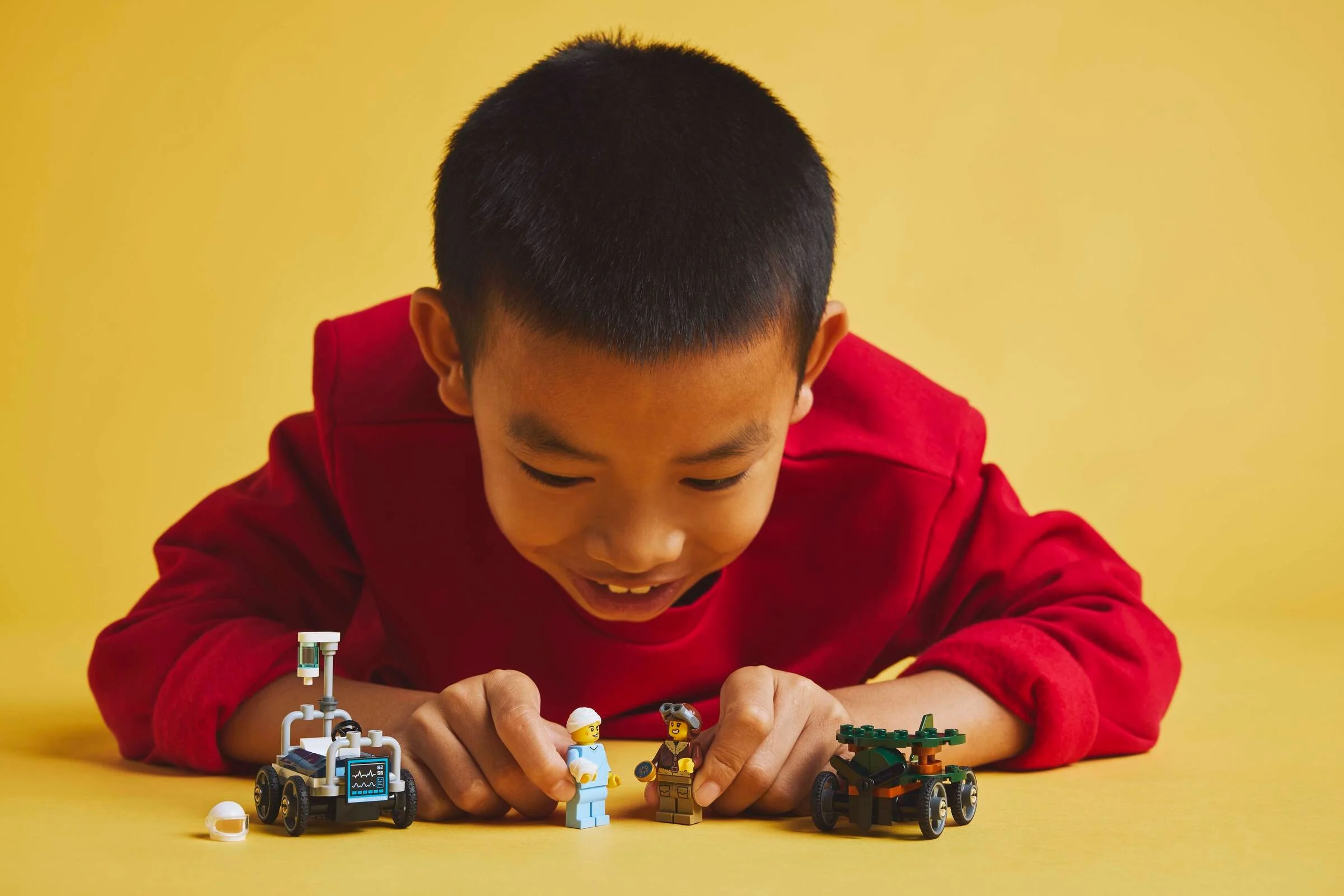 Un copil se joacă cu setul LEGO „Avion contra Mașină de Curse Pat de Spital”.