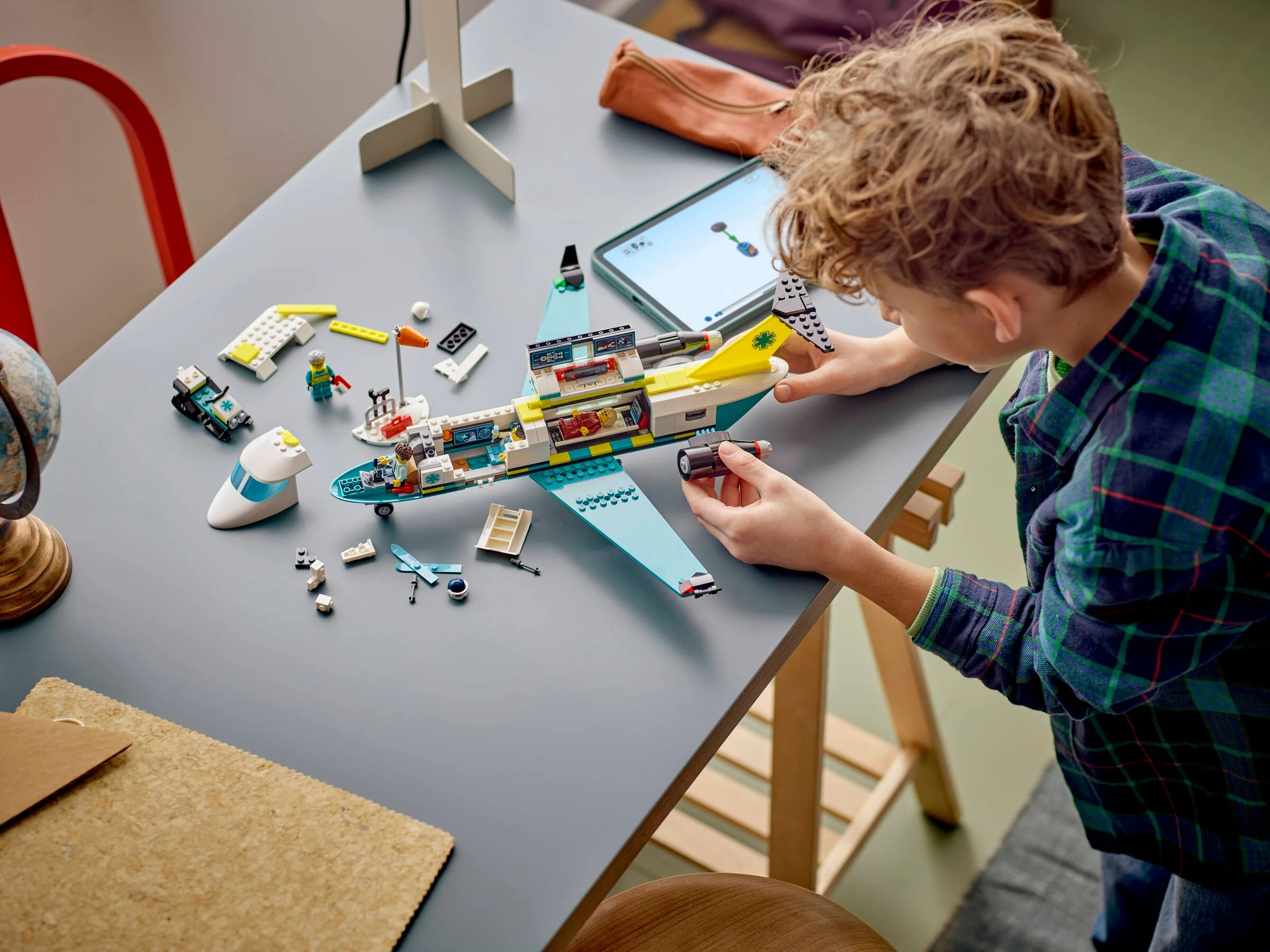 Un copil construiește avionul de salvare LEGO, urmând instrucțiunile de pe tabletă.