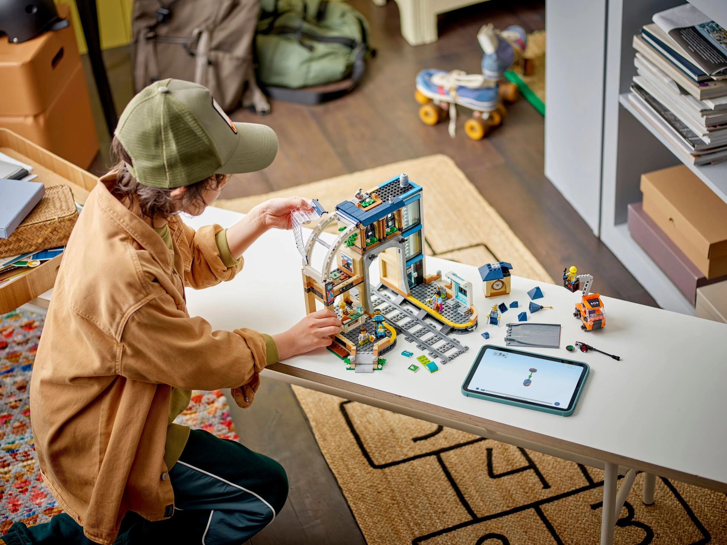 Copil construind gara LEGO. Setul include minifigurine și detalii realiste.