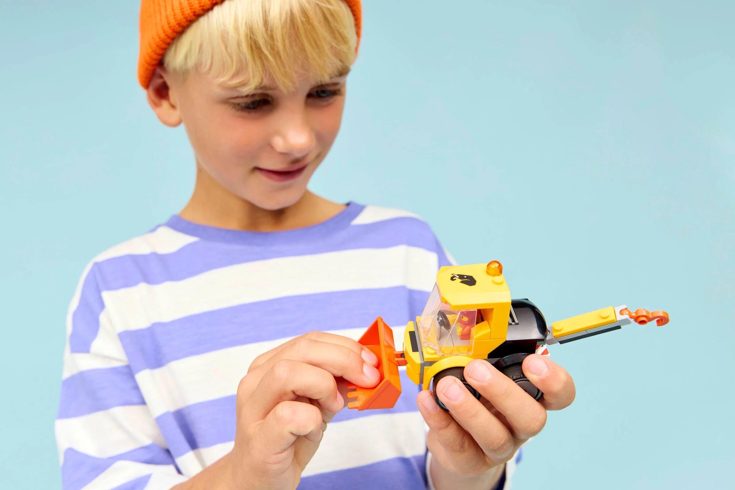 Băiat ține în mâini modelul finisat LEGO 60483 Loader, analizând detaliile construcției.