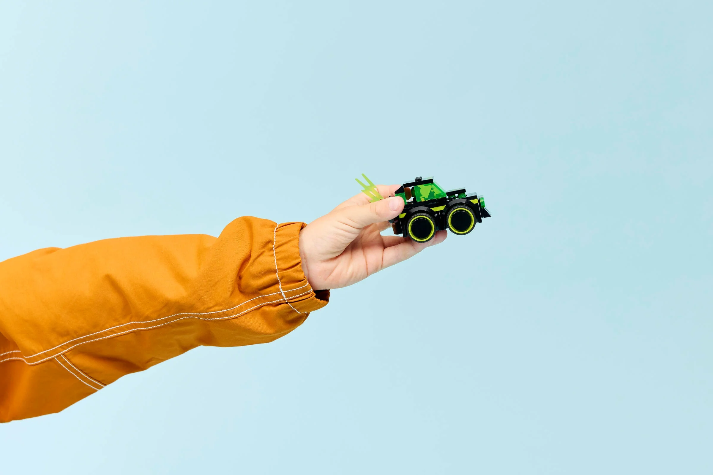 Mână ținând mașinuța LEGO Gaming Car. Jucărie atractivă, fundal albastru.